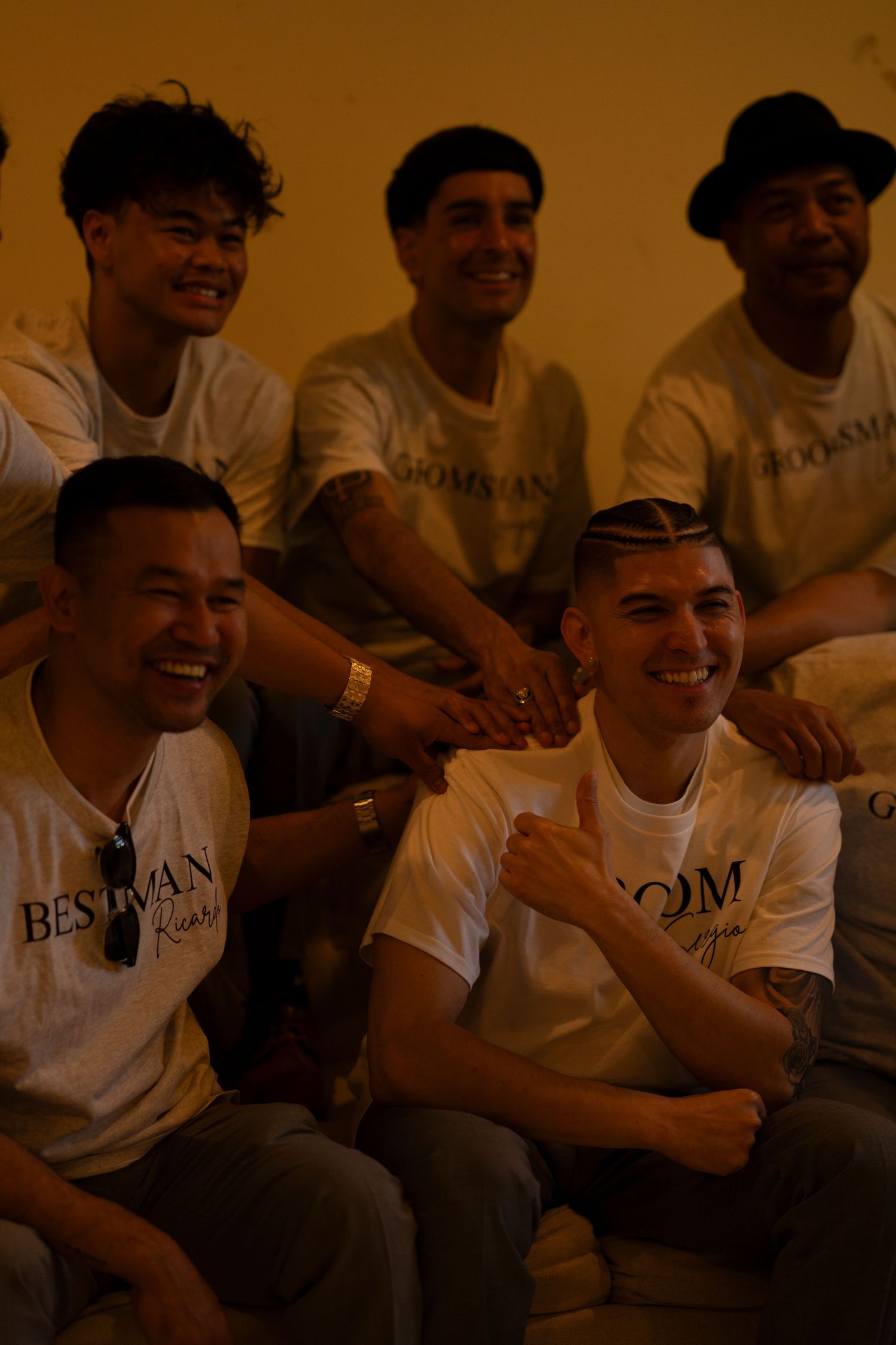 Group of groomsmen and best man smiling in matching white t-shirts at a wedding celebration.