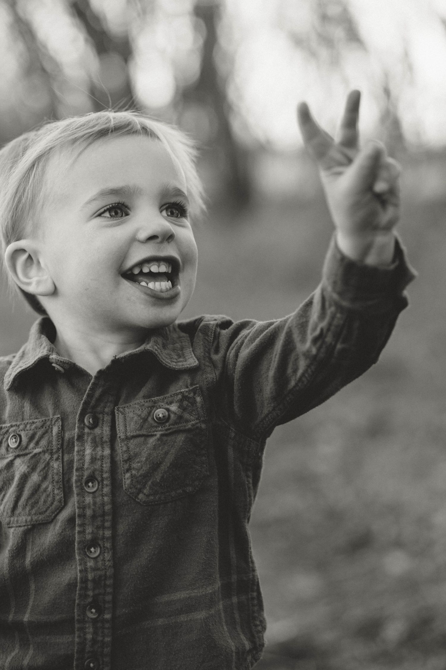 Happy blonde toddler boy in plaid shirt pointing upward in black and white outdoor portrait.