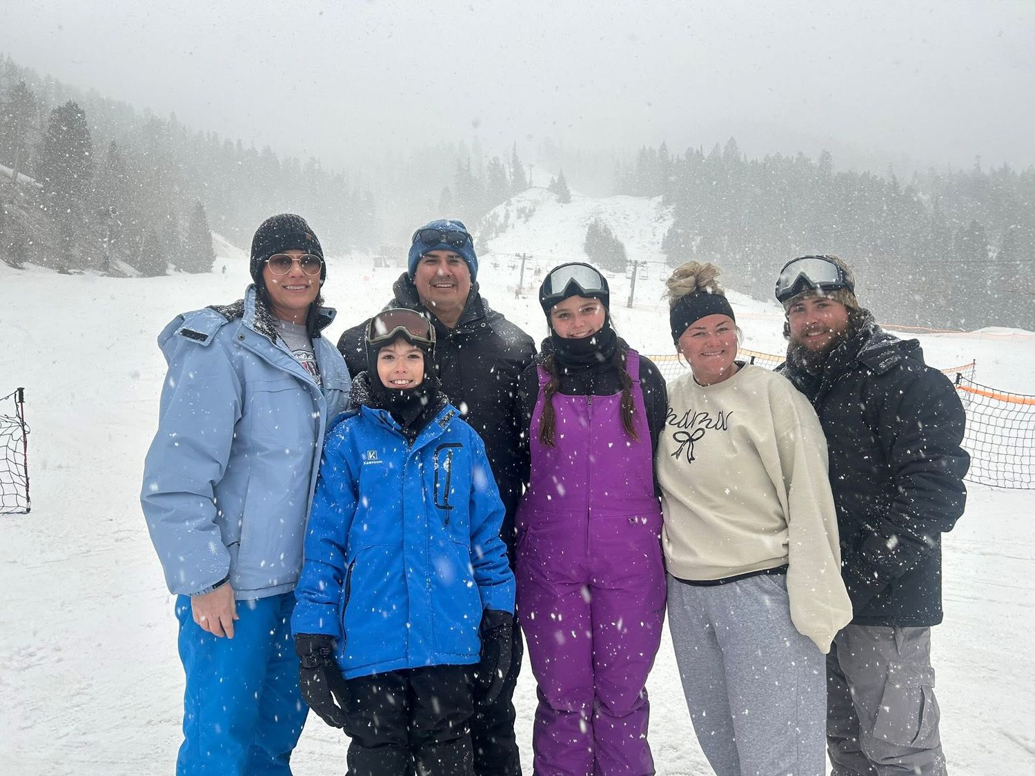 Group of six people posing together on a snowy ski slope in winter gear.