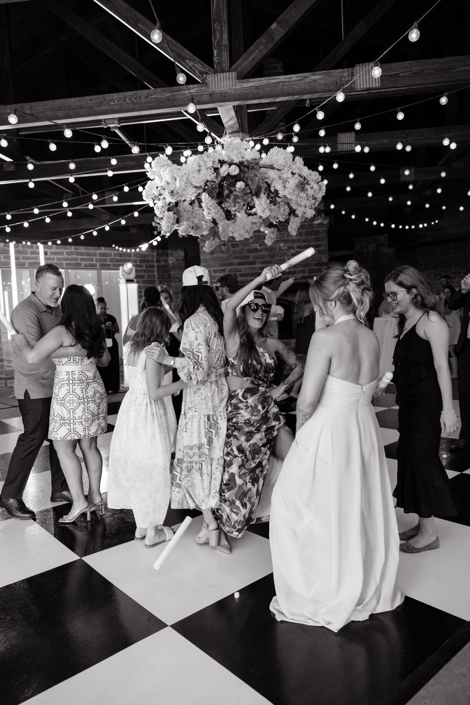 Black and white photo of guests dancing on checkered floor at elegant wedding reception.