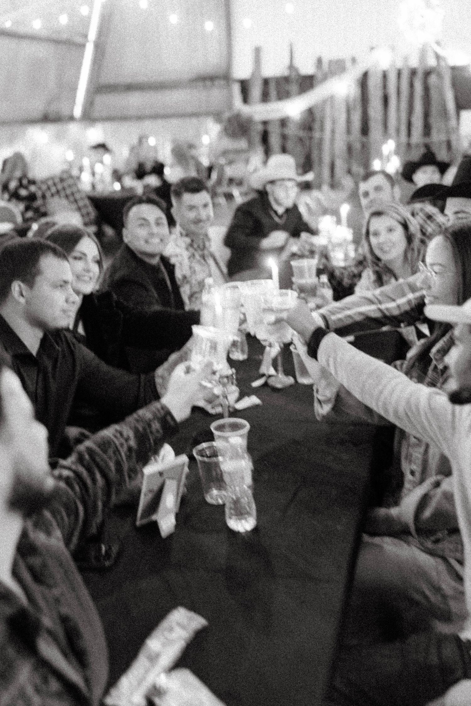 Black and white photo of wedding guests clinking glasses in a celebratory toast at a reception.