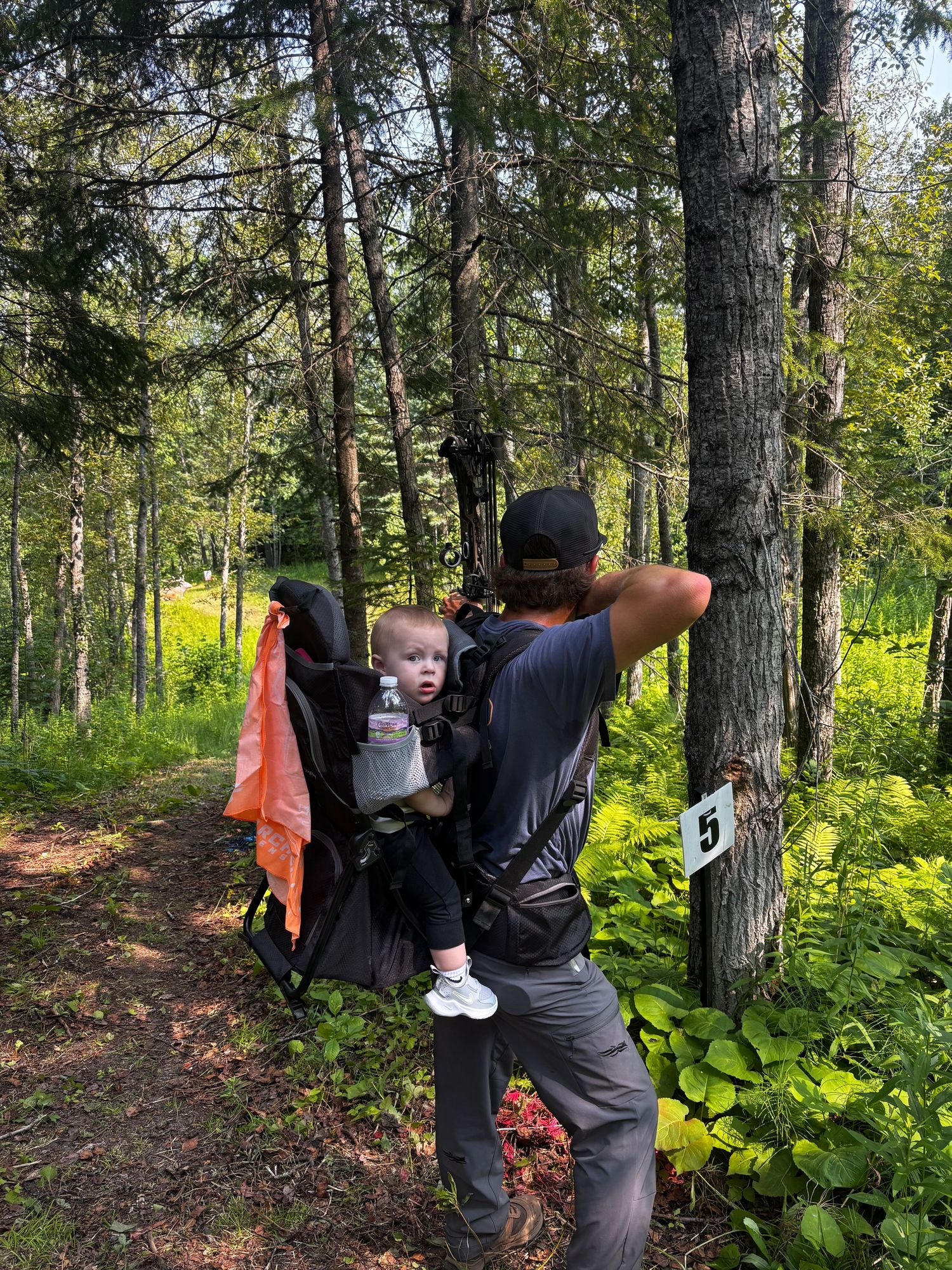 Father carrying baby in backpack carrier on a forest hiking trail in summer.