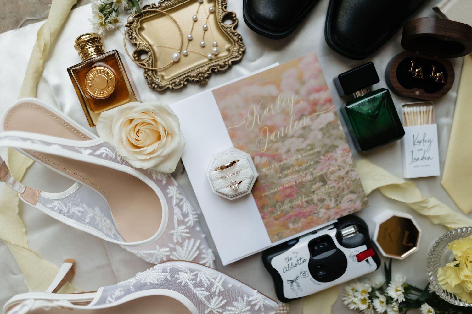 Elegant wedding flat lay featuring bridal heels, bouquet, rings, perfume, and disposable camera.