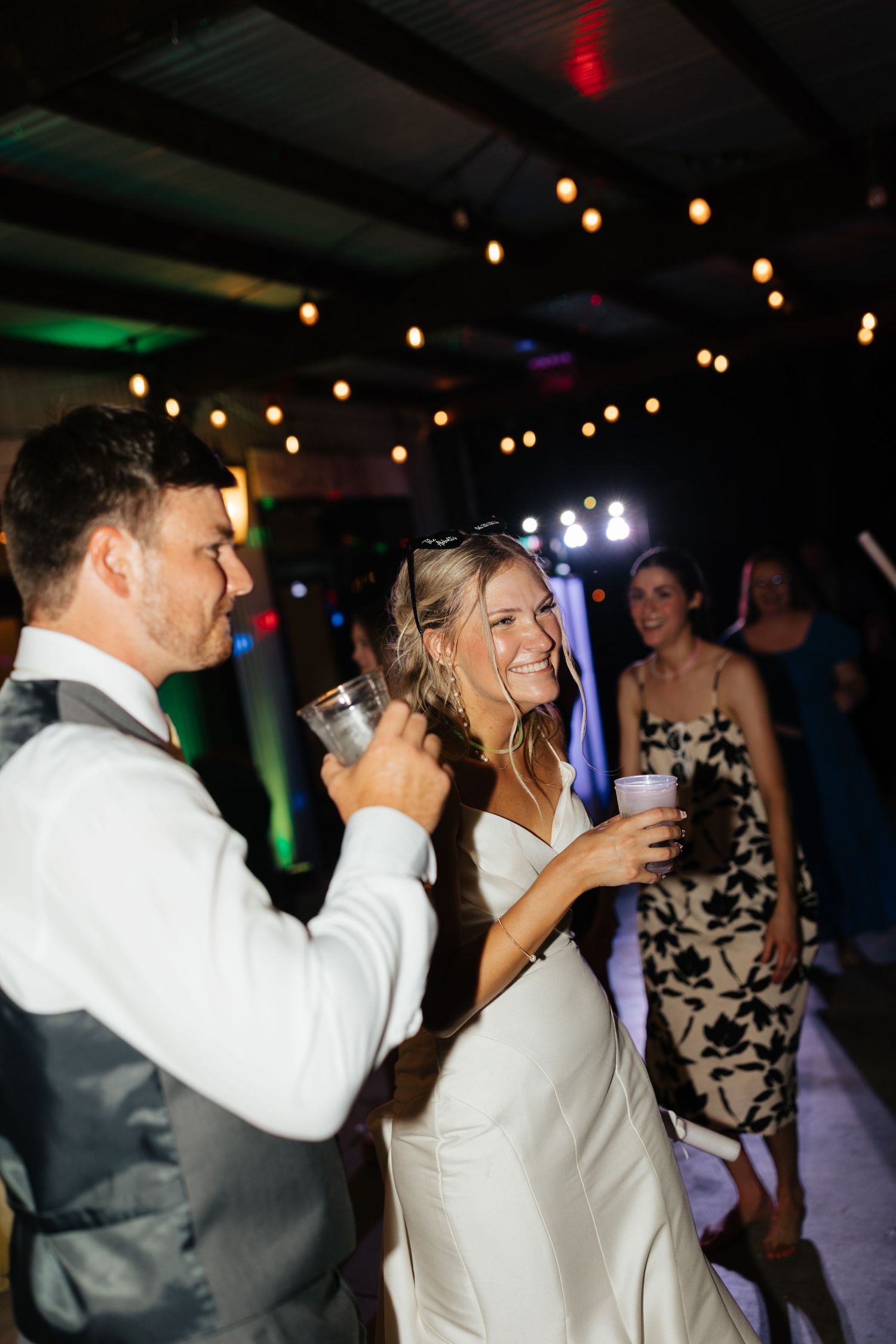 Bride and groom laughing and dancing together with drinks at lively wedding reception celebration.