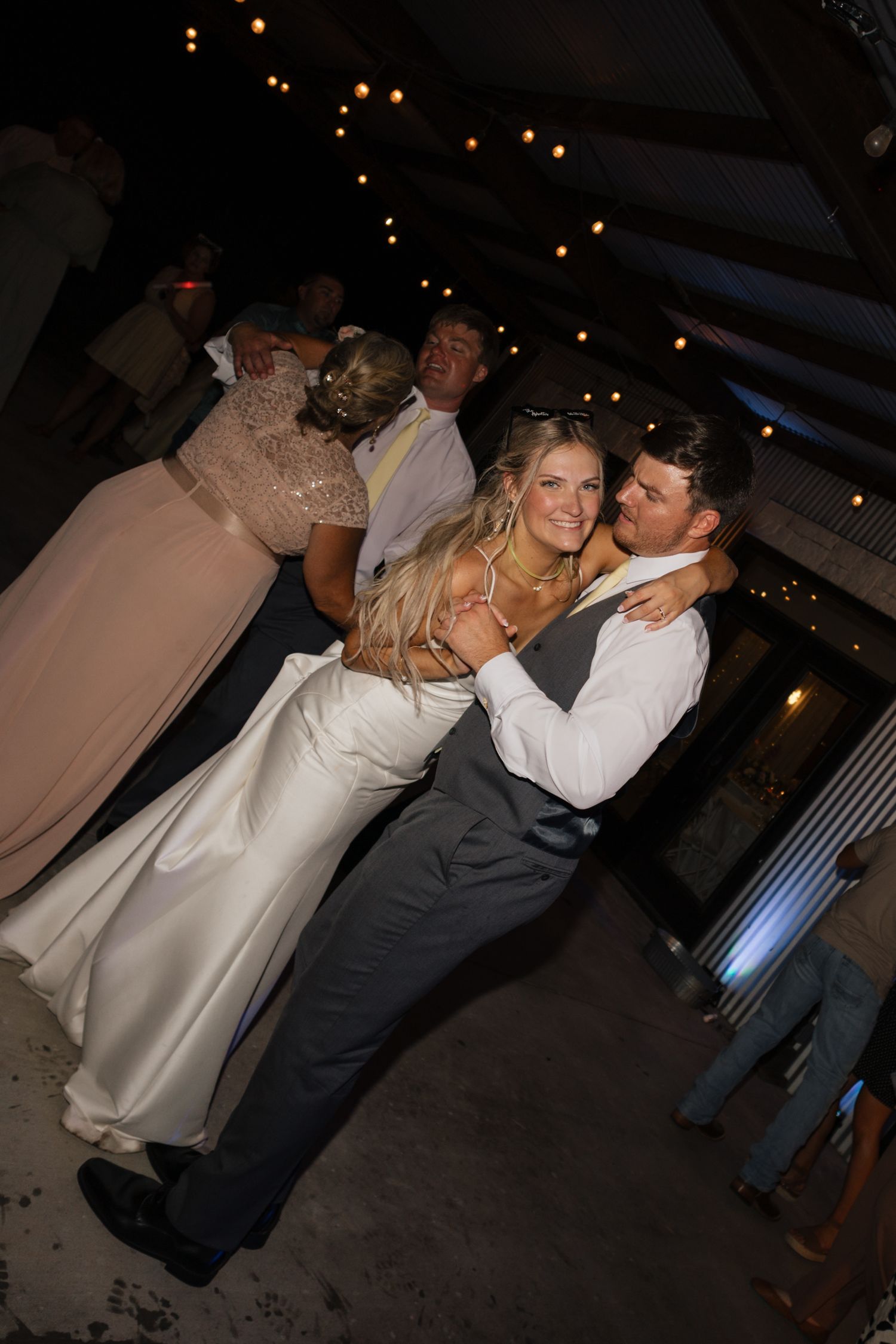 Bride and groom share a romantic dance at their wedding reception under warm string lights.