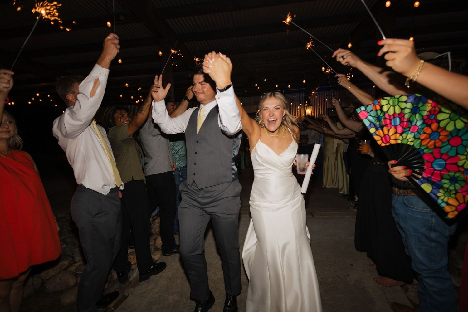 Bride and groom celebrating joyful sparkler exit surrounded by cheering wedding guests at night.