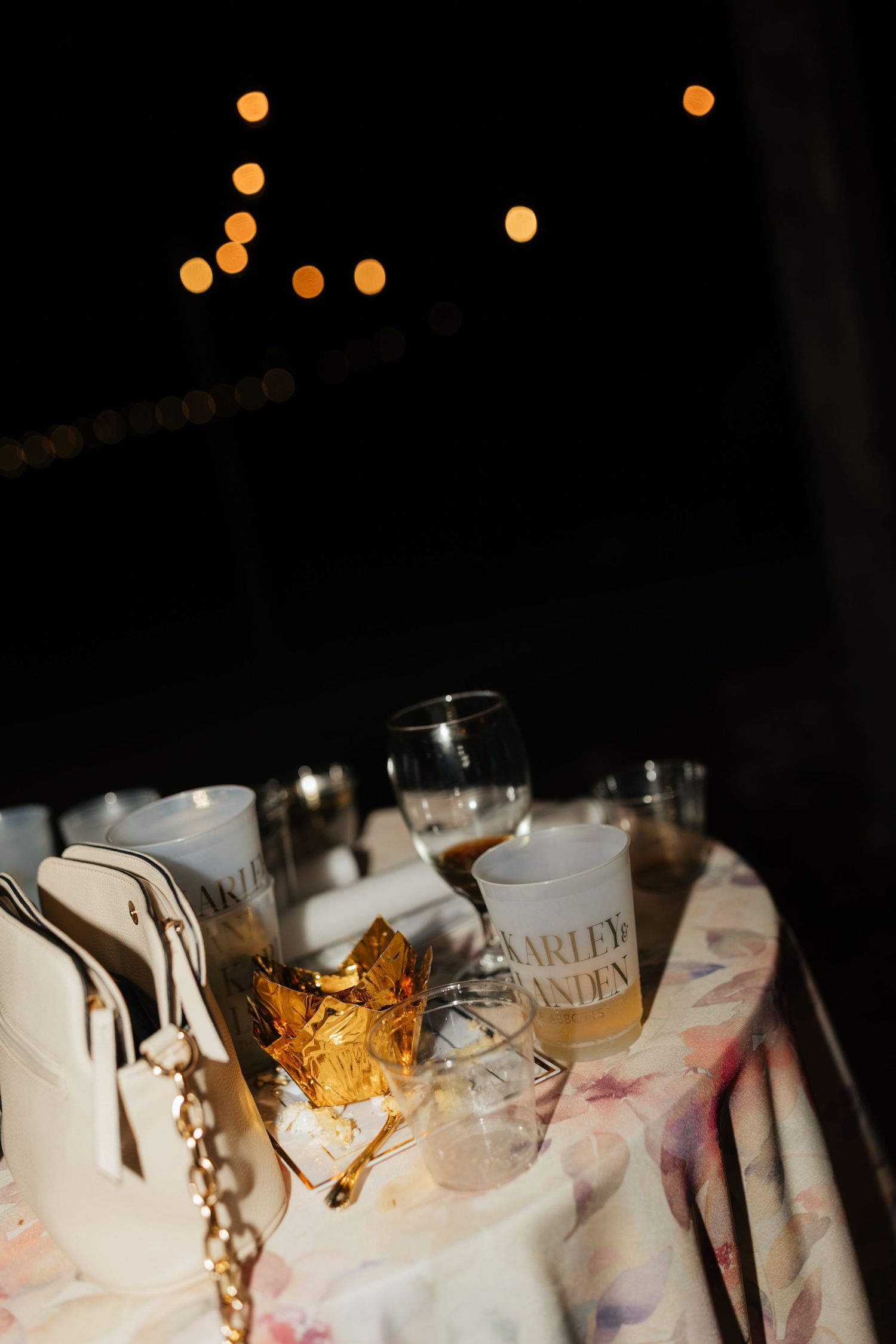 Personalized frosted wedding cups and candles on table with bokeh string lights at reception.