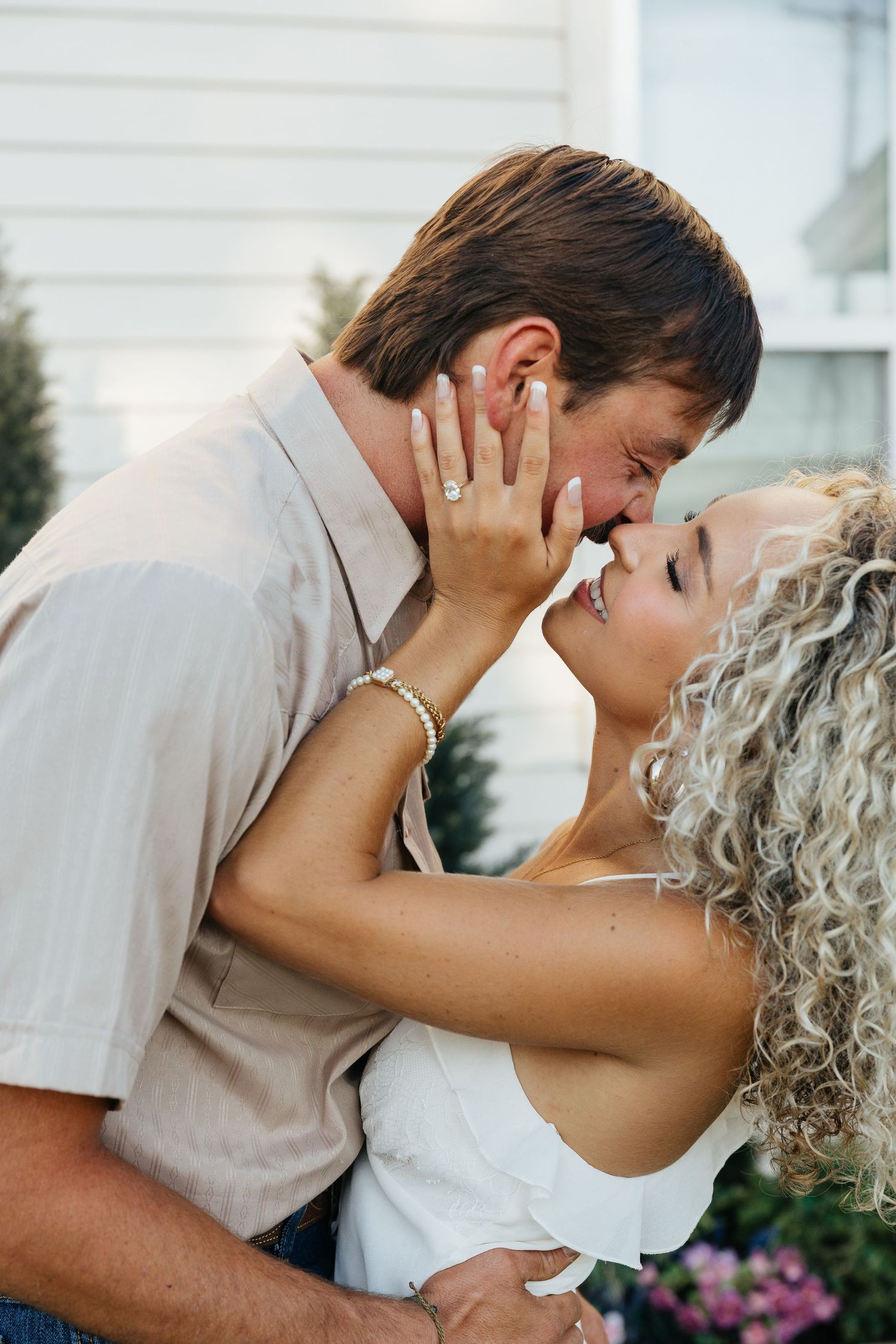 Couple sharing a romantic kiss outdoors during their engagement session, woman showing off diamond ring.