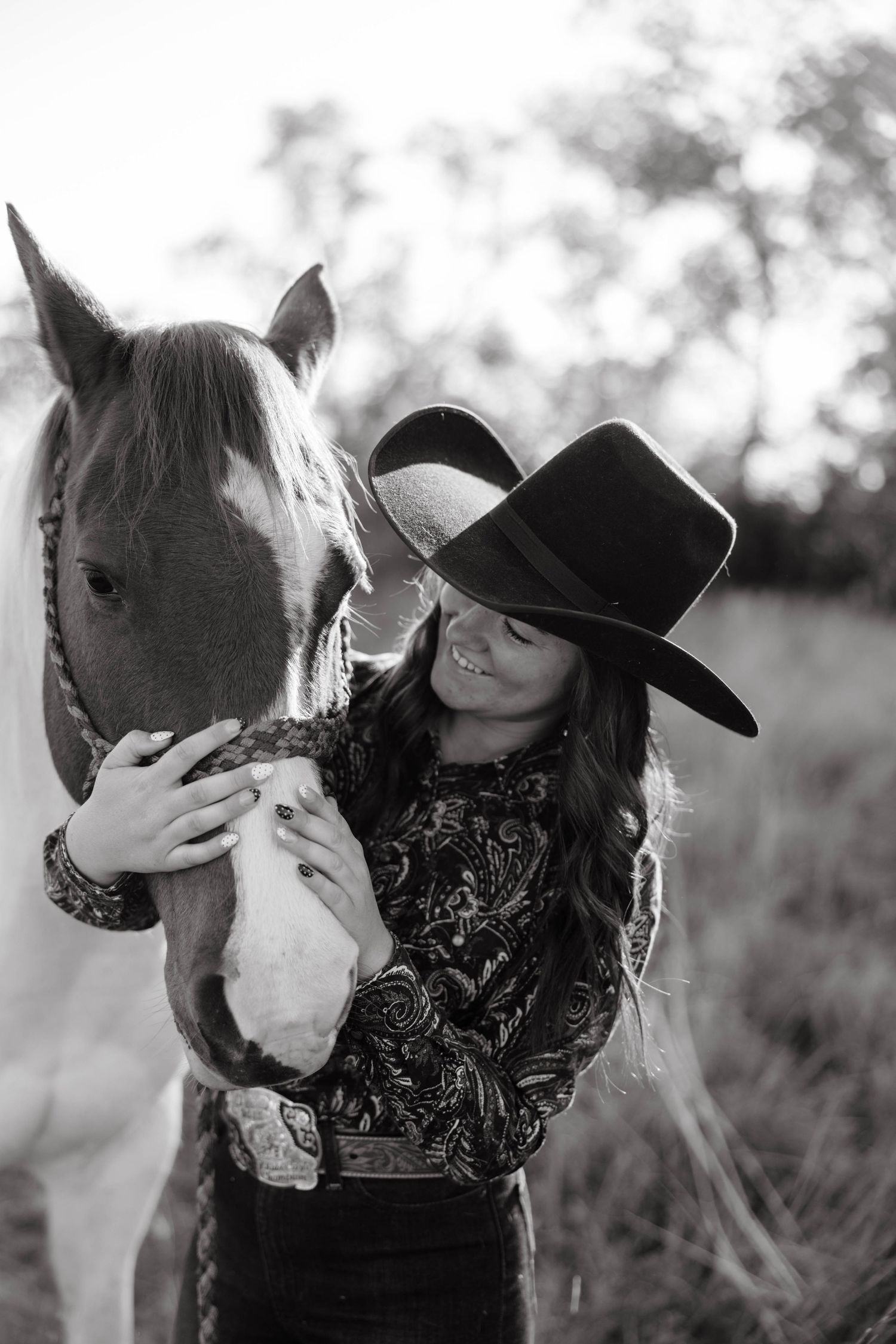 Black and white portrait of woman in cowboy hat affectionately embracing a horse.