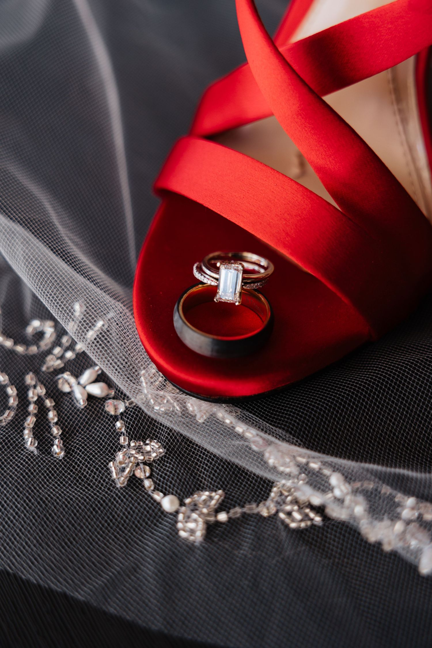Diamond engagement ring and wedding band nestled in red satin bridal heel with jeweled veil.