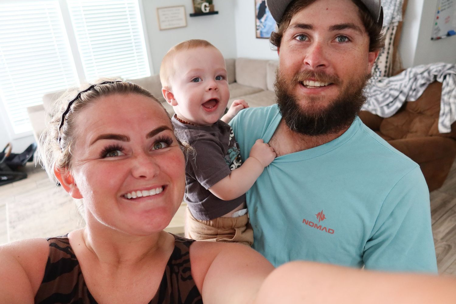 Happy family selfie with couple and laughing baby in a bright living room.