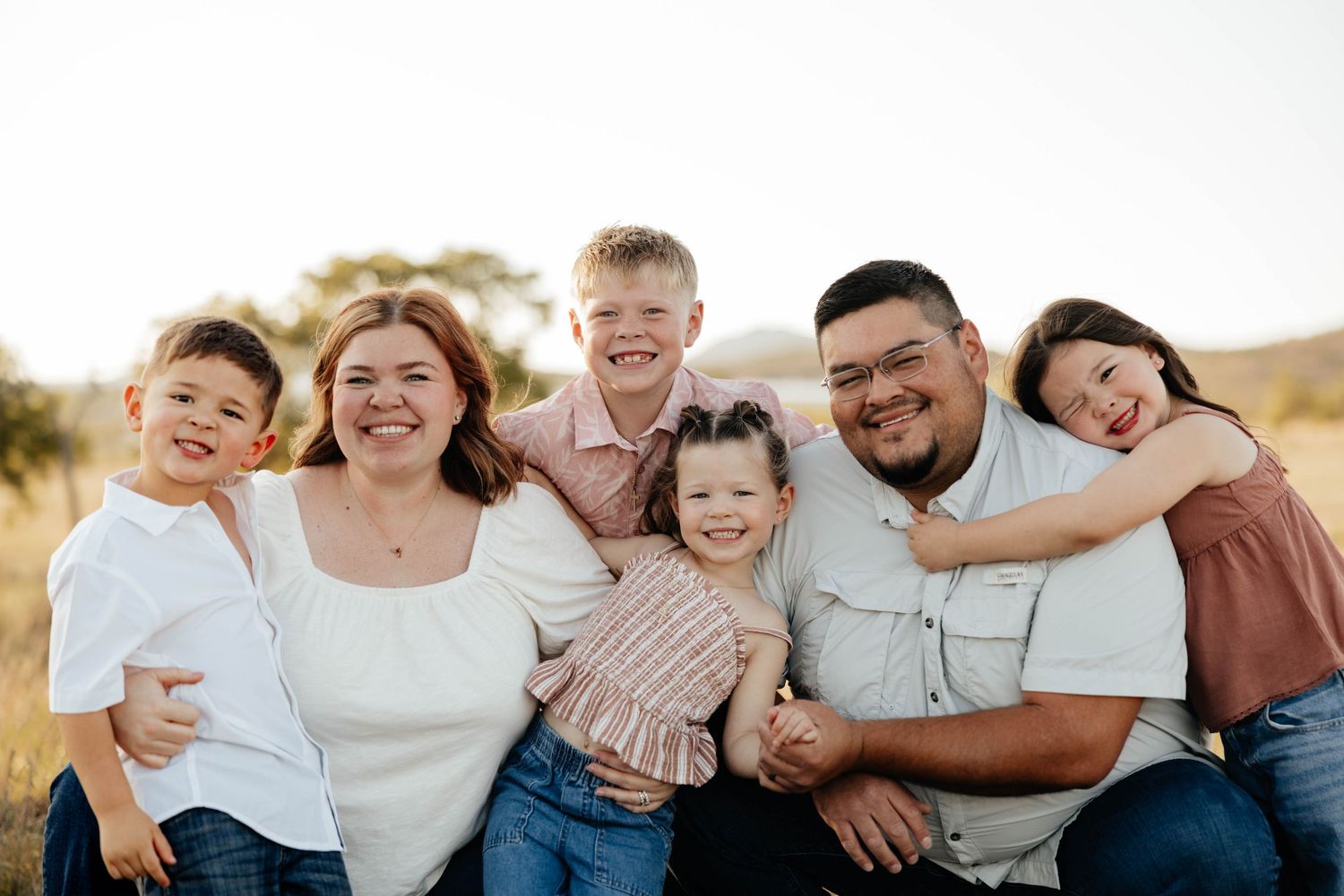 Happy family of six smiling together in a sunny golden field at sunset.