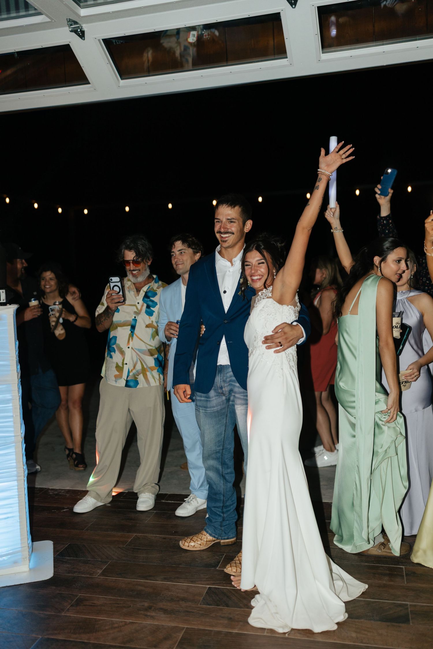 A bride raises her arm in celebration with her groom and guests on the dance floor.