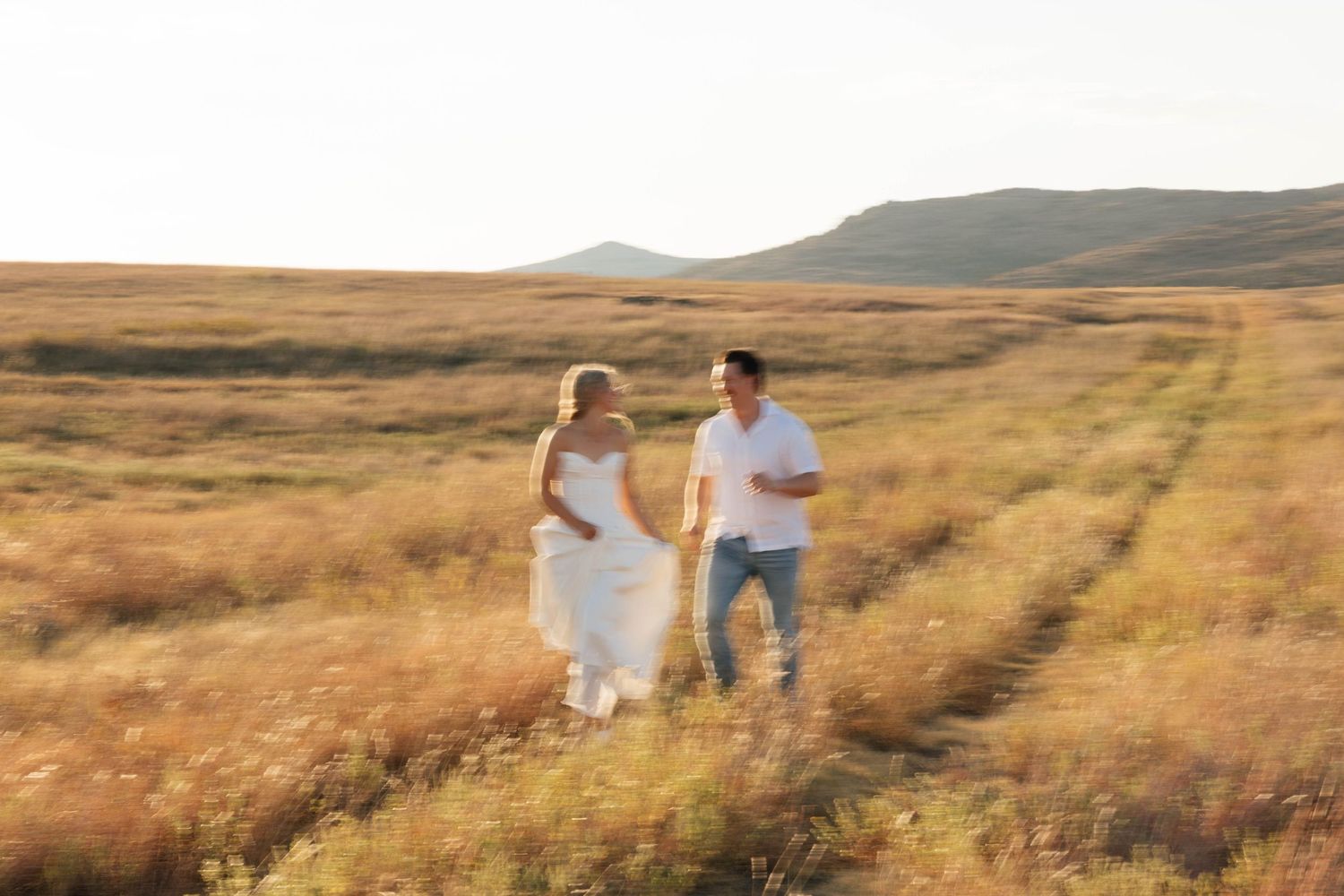 A joyful couple runs hand in hand through a golden field at sunset.