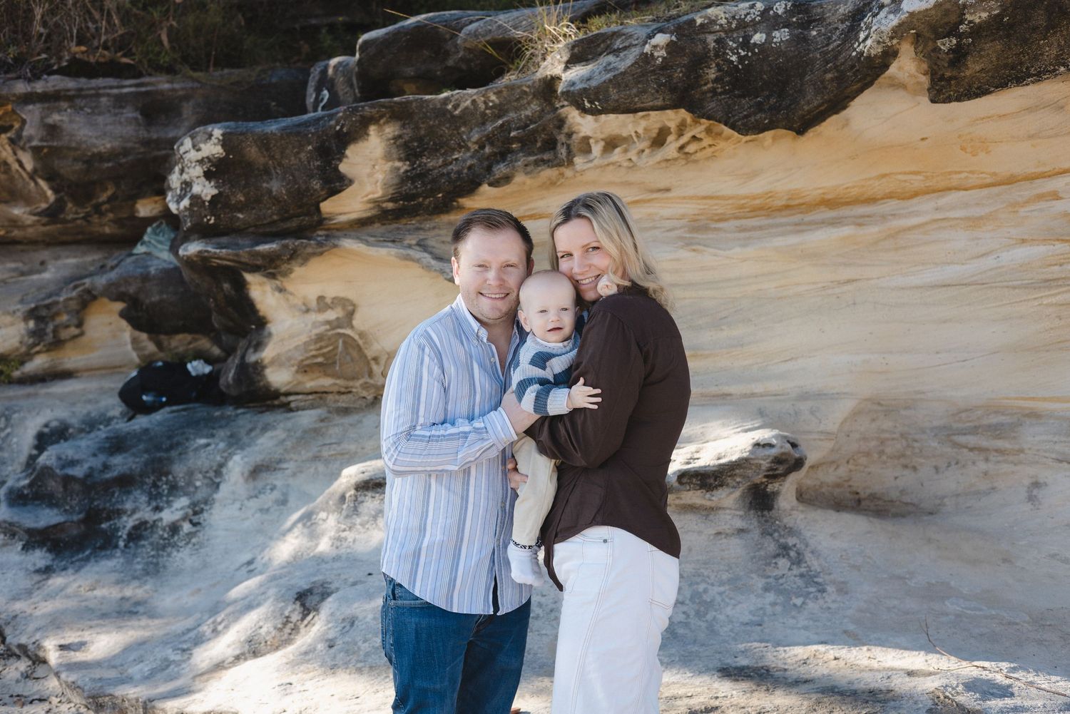 Happy family with baby posing outdoors near scenic sandstone rock formations on a sunny day.