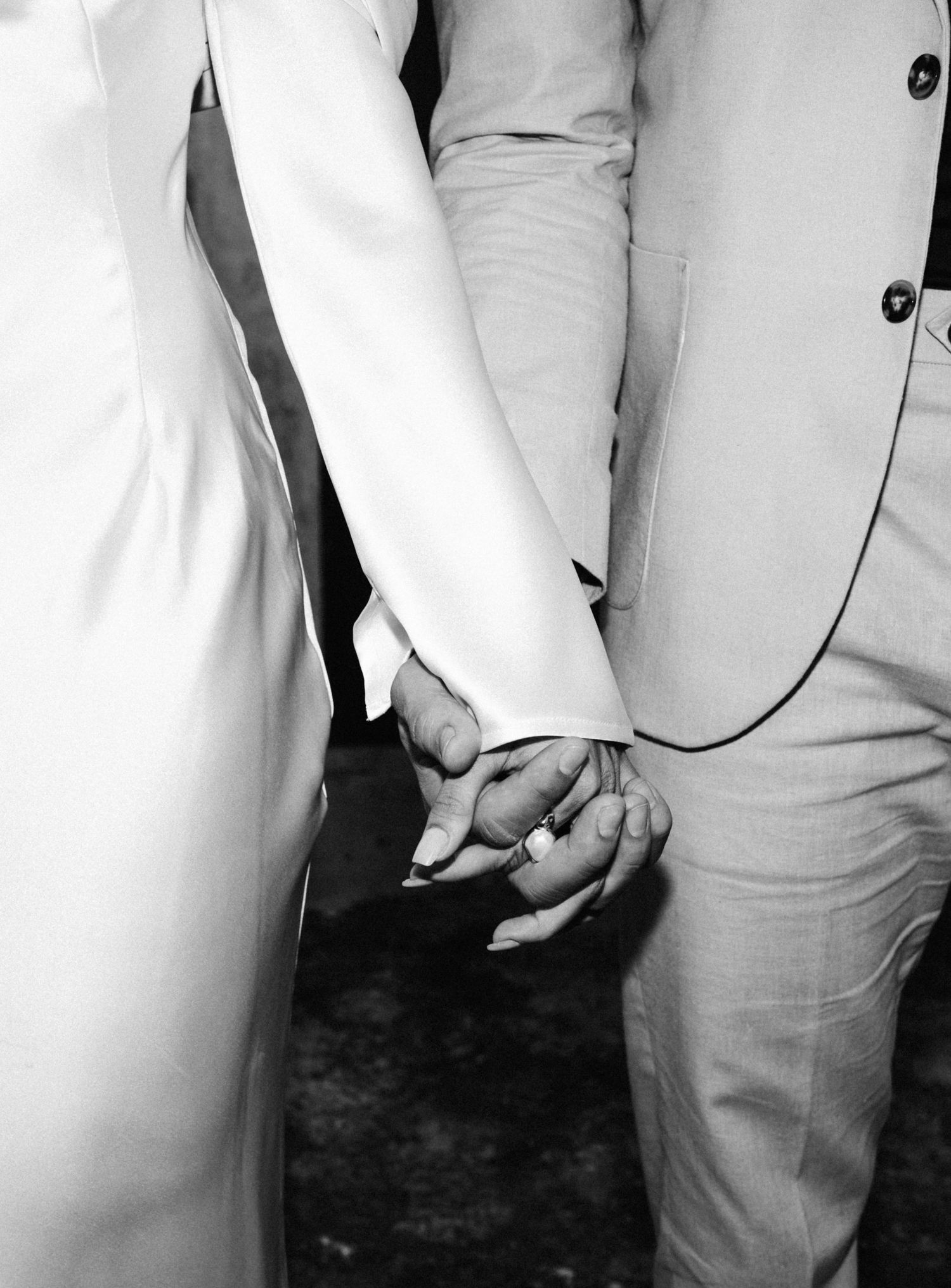 Close-up black and white photo of bride and groom holding hands, showing wedding ring details.