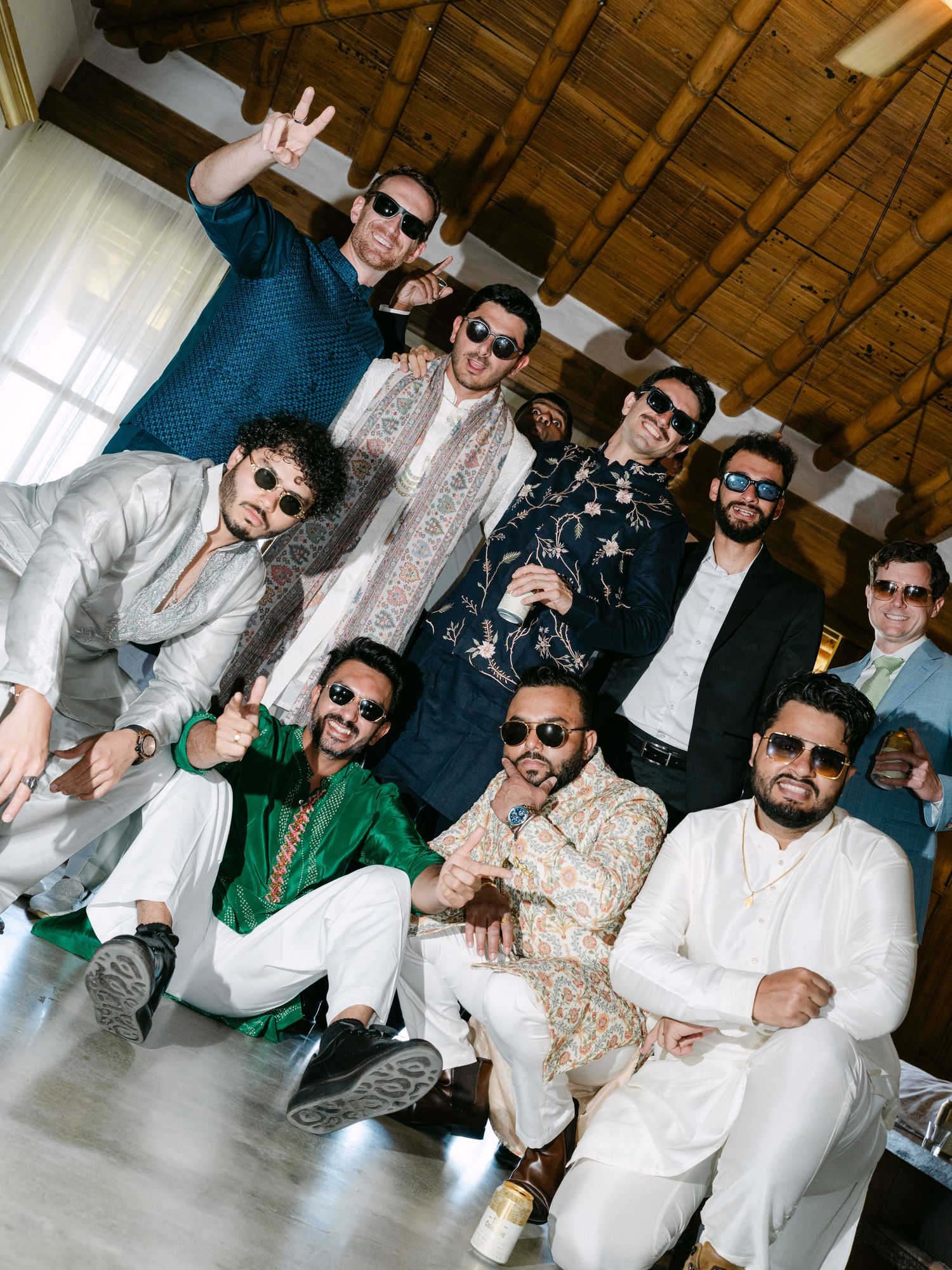 Group of men in traditional Indian attire and sunglasses posing together at a wedding celebration.