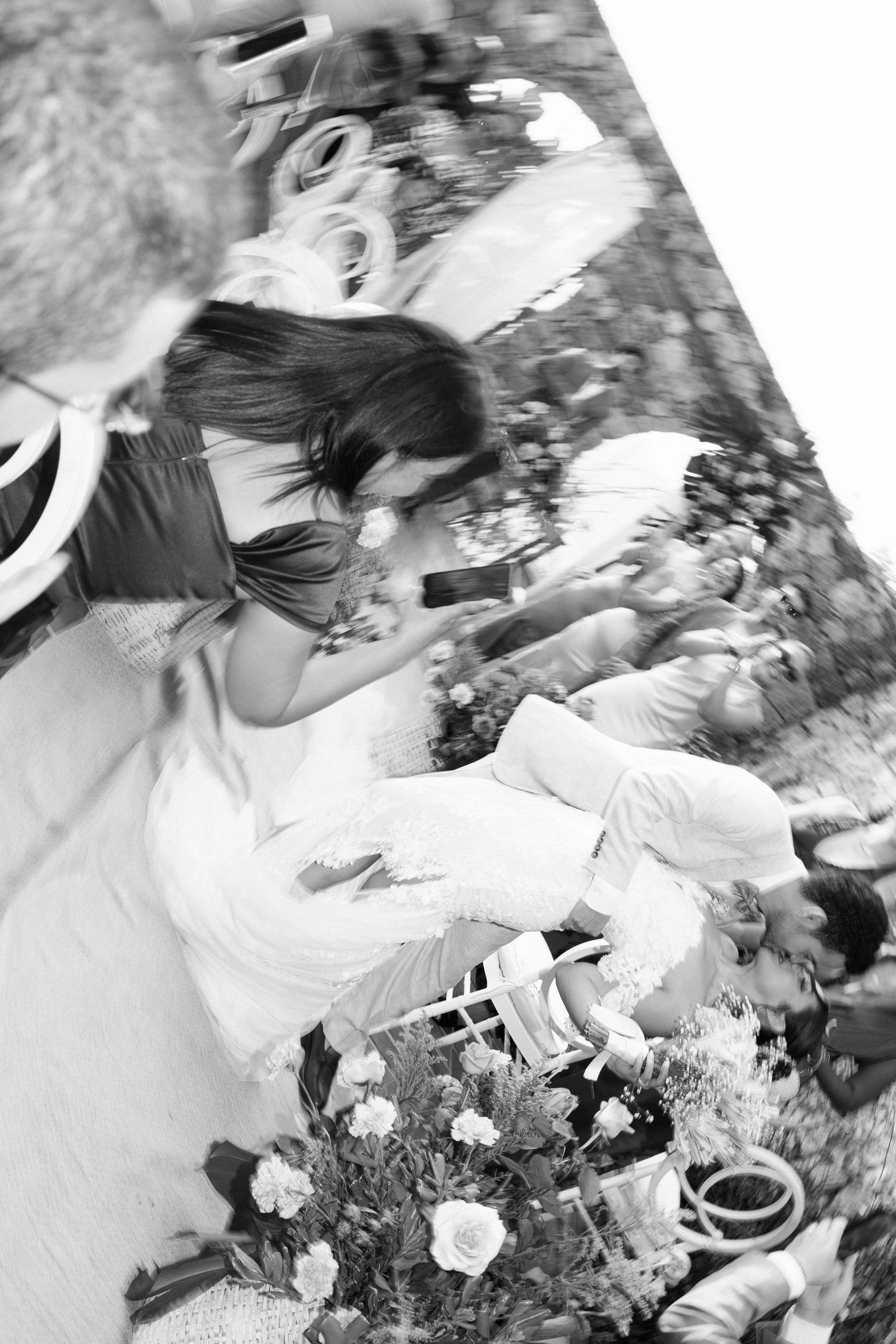 Black and white overhead shot of bride and groom seated at wedding reception table with flowers.