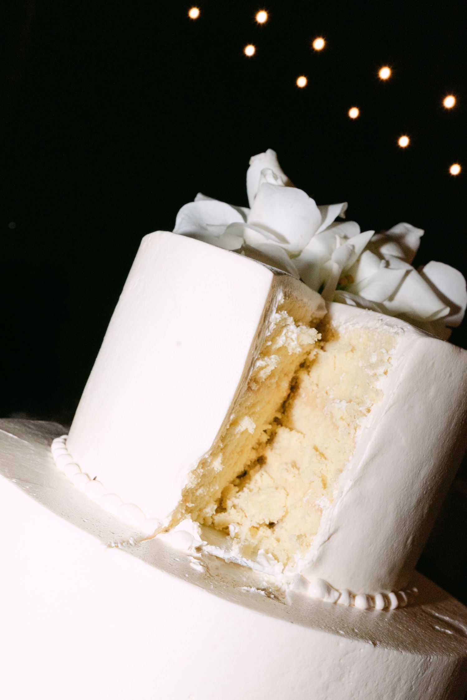 White two-tier wedding cake with floral topper with a slice removed revealing yellow interior.