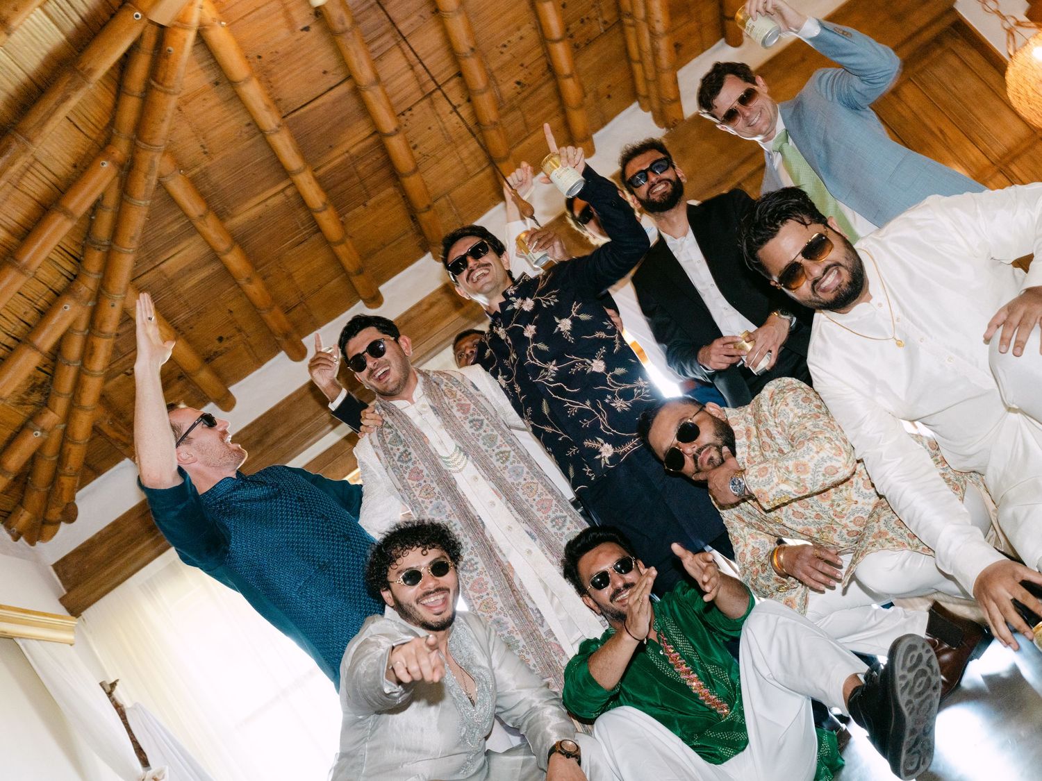 Groom celebrating with groomsmen in traditional South Asian wedding attire under a rustic wooden ceiling.