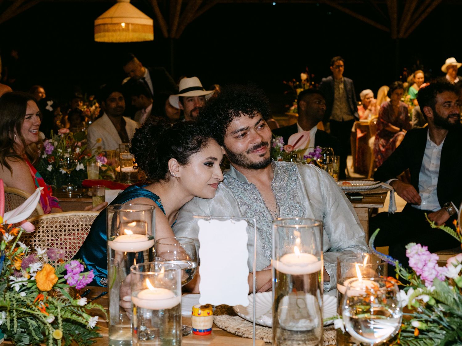 Couple sharing an intimate moment at a candlelit wedding reception table surrounded by colorful floral arrangements.
