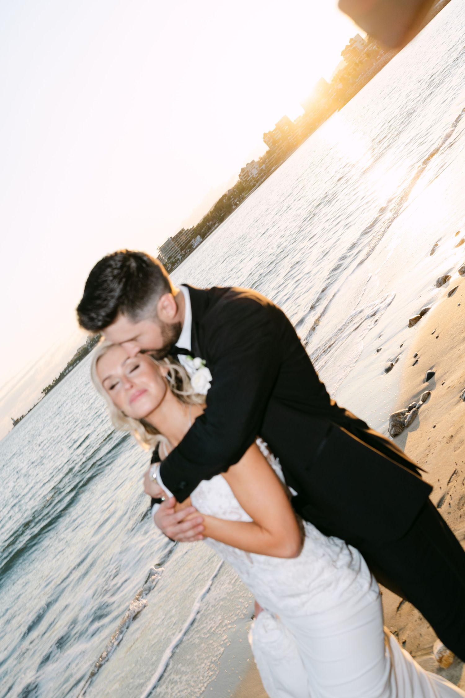 Romantic beach wedding photo of groom kissing bride while dipping her at golden hour sunset.