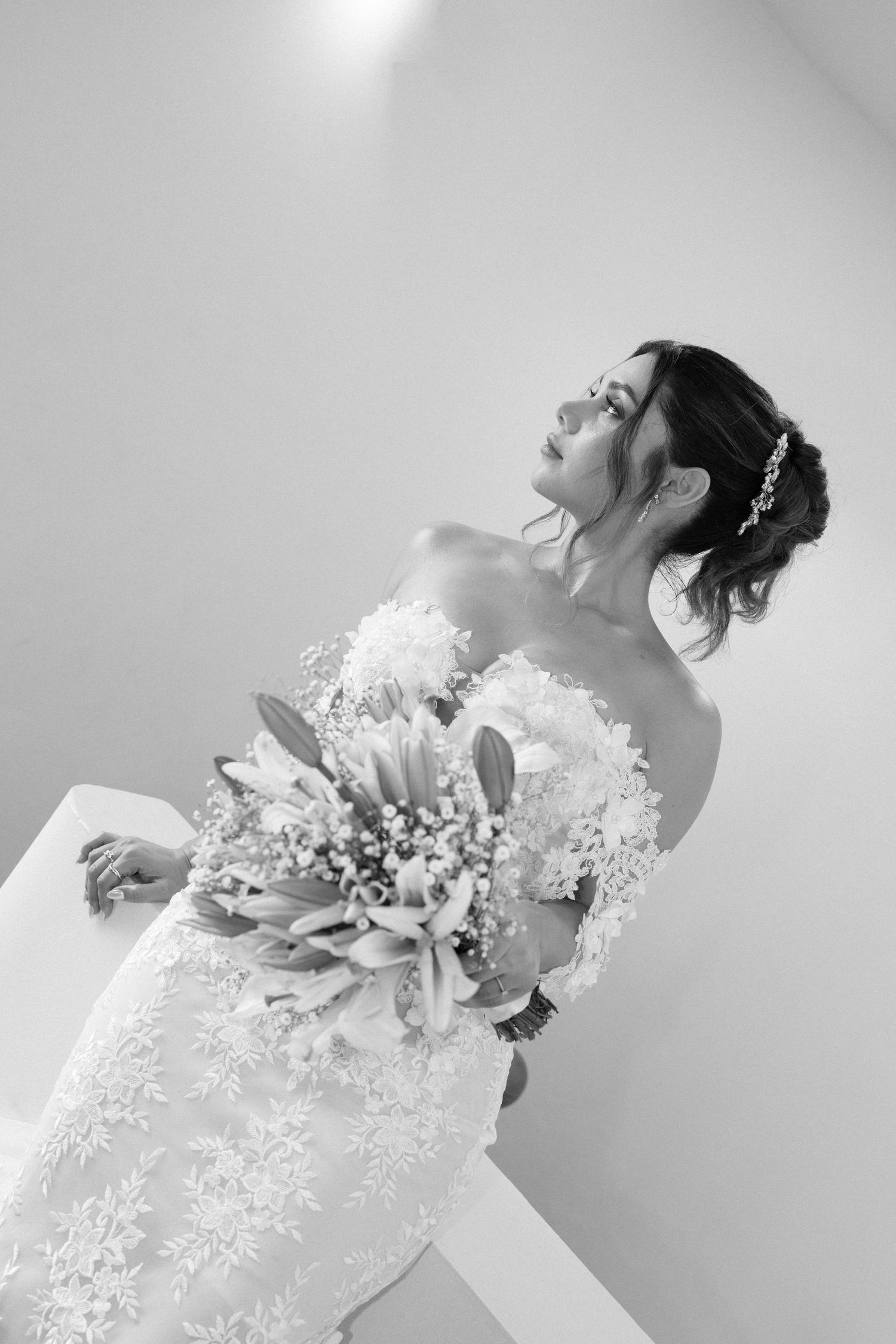 Black and white portrait of bride in lace wedding gown holding floral bouquet.