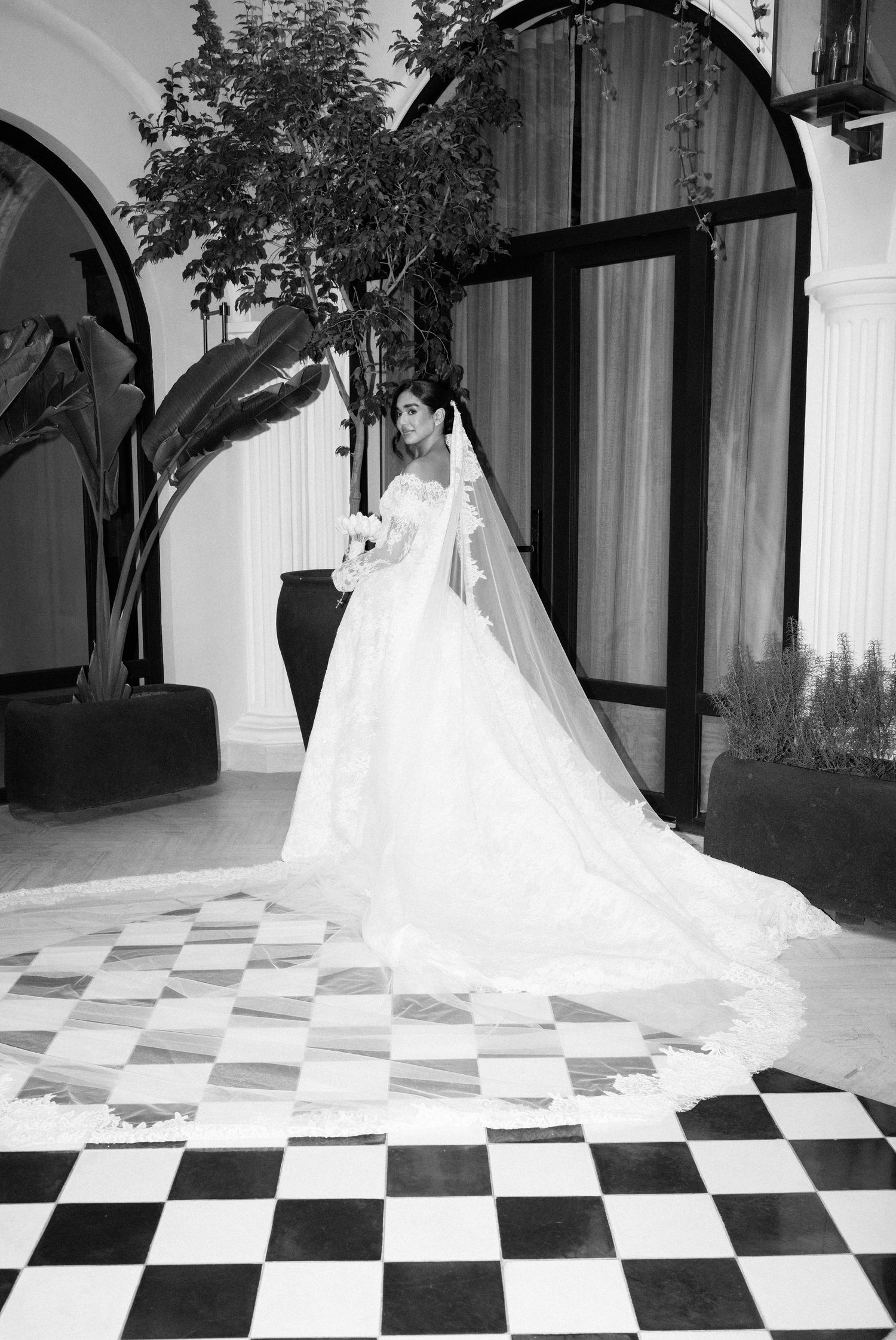 Bride in a stunning ball gown wedding dress with long veil on black and white checkered floor in elegant venue.
