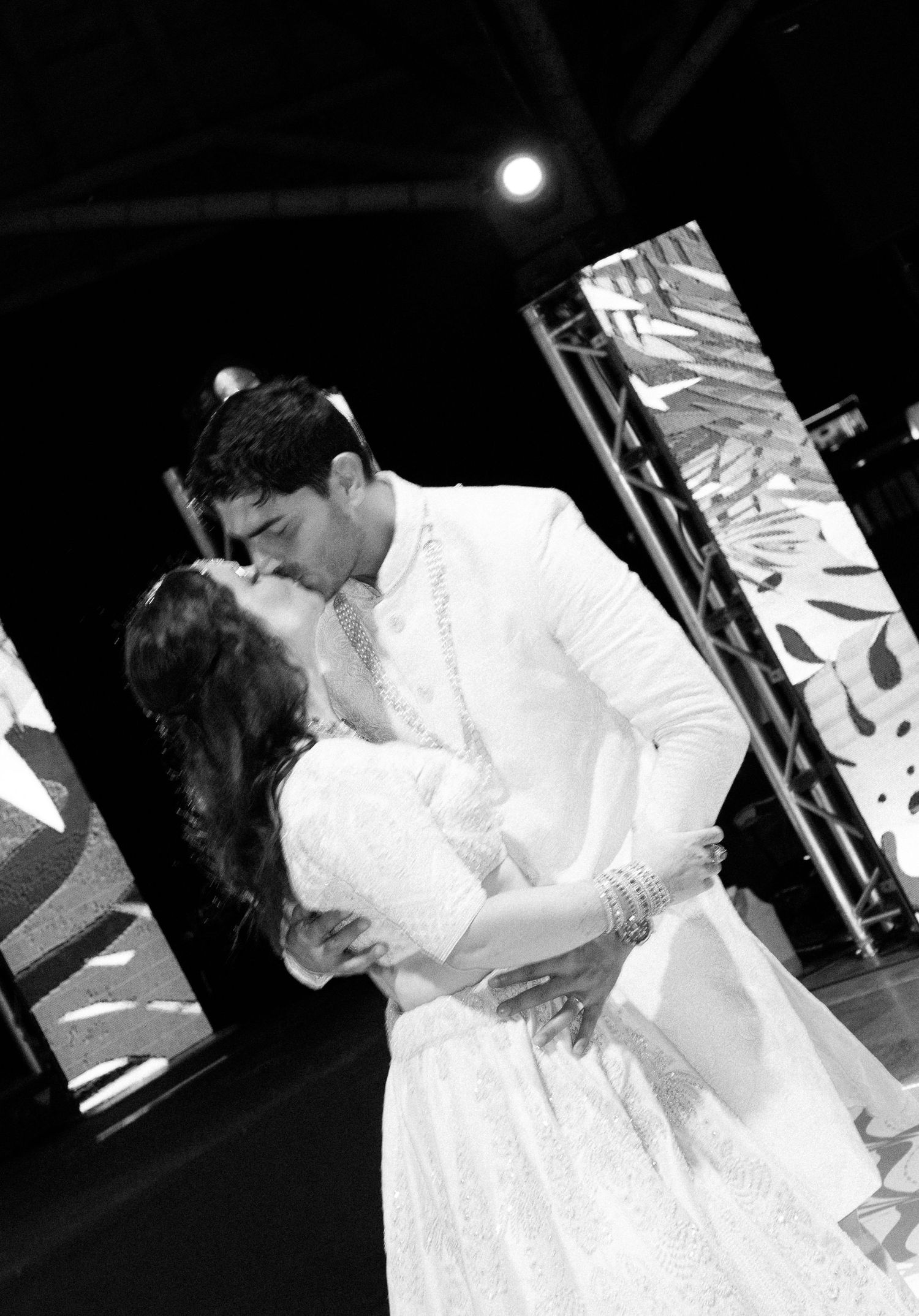 Bride and groom sharing first dance kiss in black and white photo at elegant wedding reception stage.