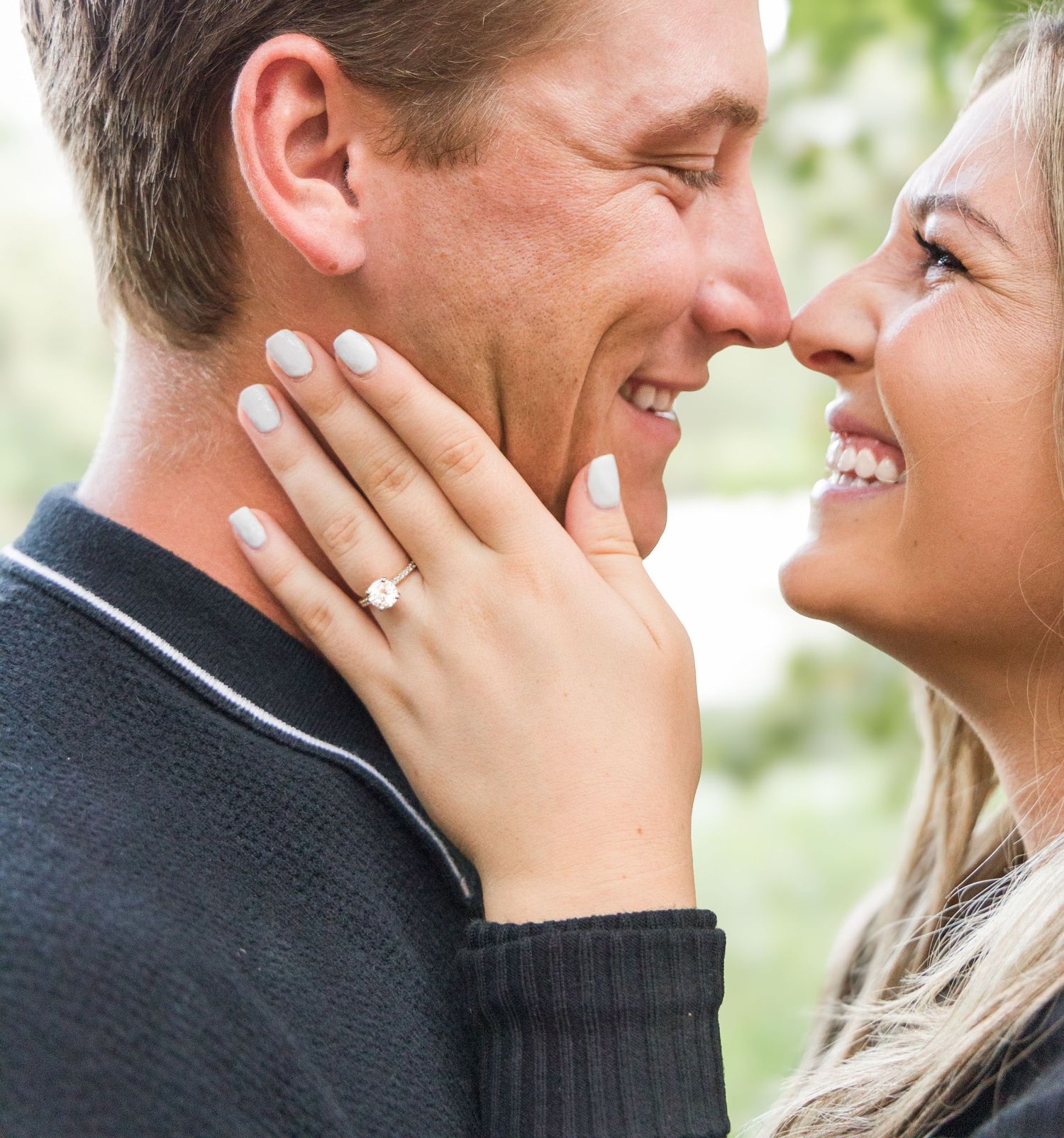 Happy couple laughing nose to nose as the woman's hand shows off a sparkling diamond engagement ring.