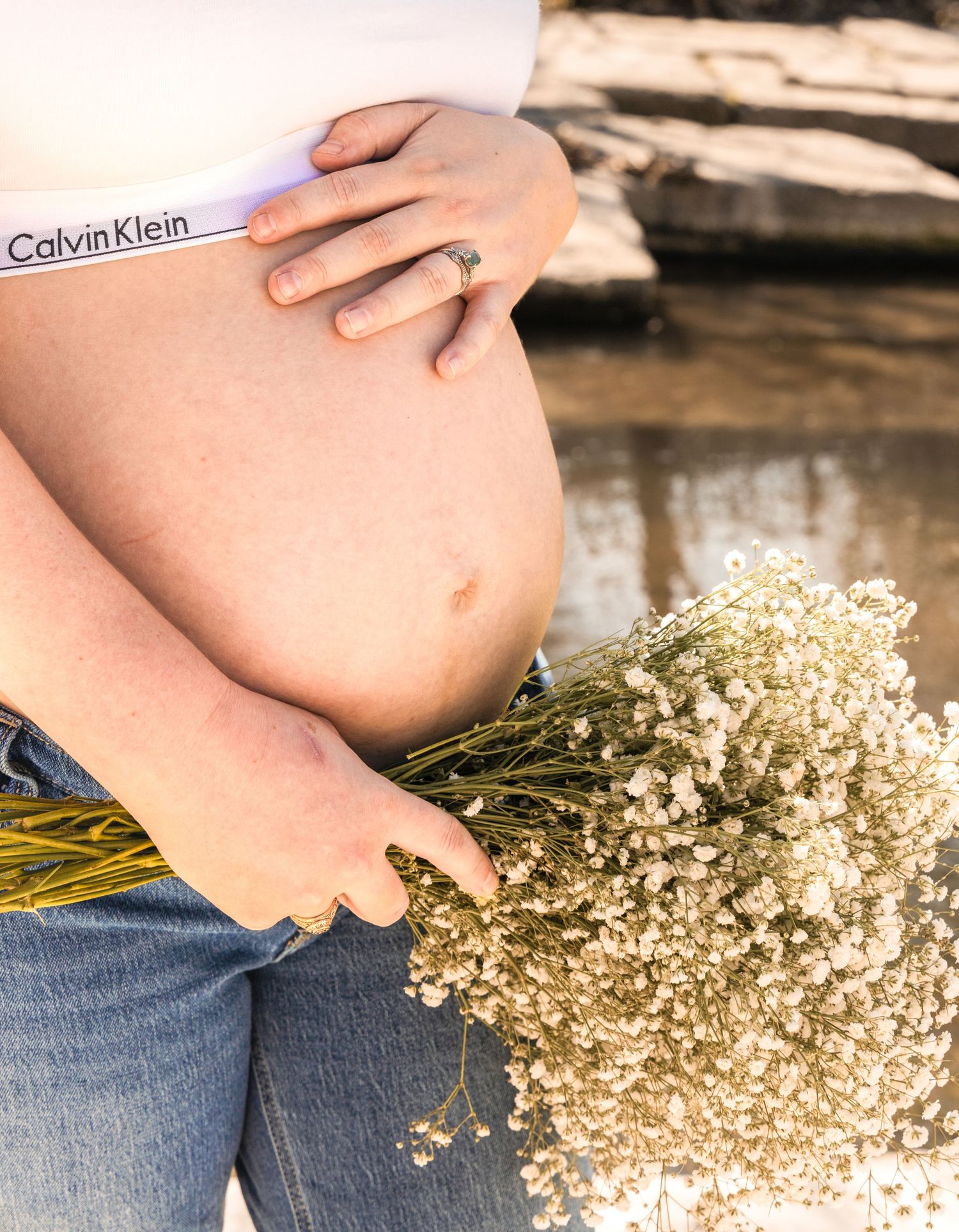 Close-up of a pregnant woman's bare belly with her hand resting on it, holding a bouquet of dried baby's breath flowers.