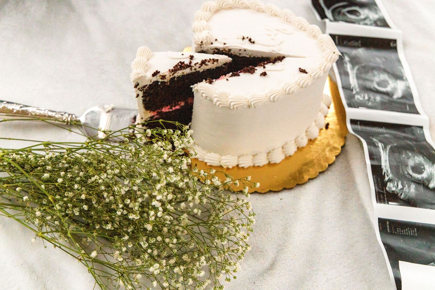 Partially sliced white frosted cake with chocolate layers beside baby's breath flowers and a strip of ultrasound images.