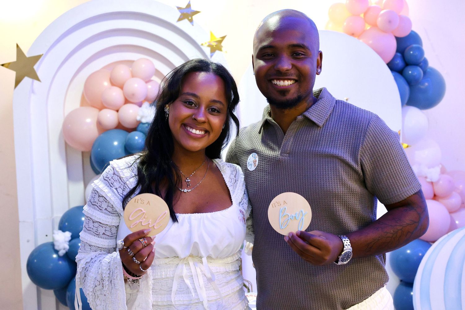 Smiling couple holding gender reveal discs at a blue and pink balloon decorated baby shower party.