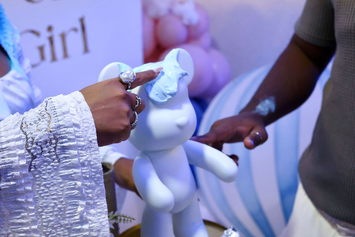 Close-up of hands touching a white bear figurine at a gender reveal party with Girl banner.