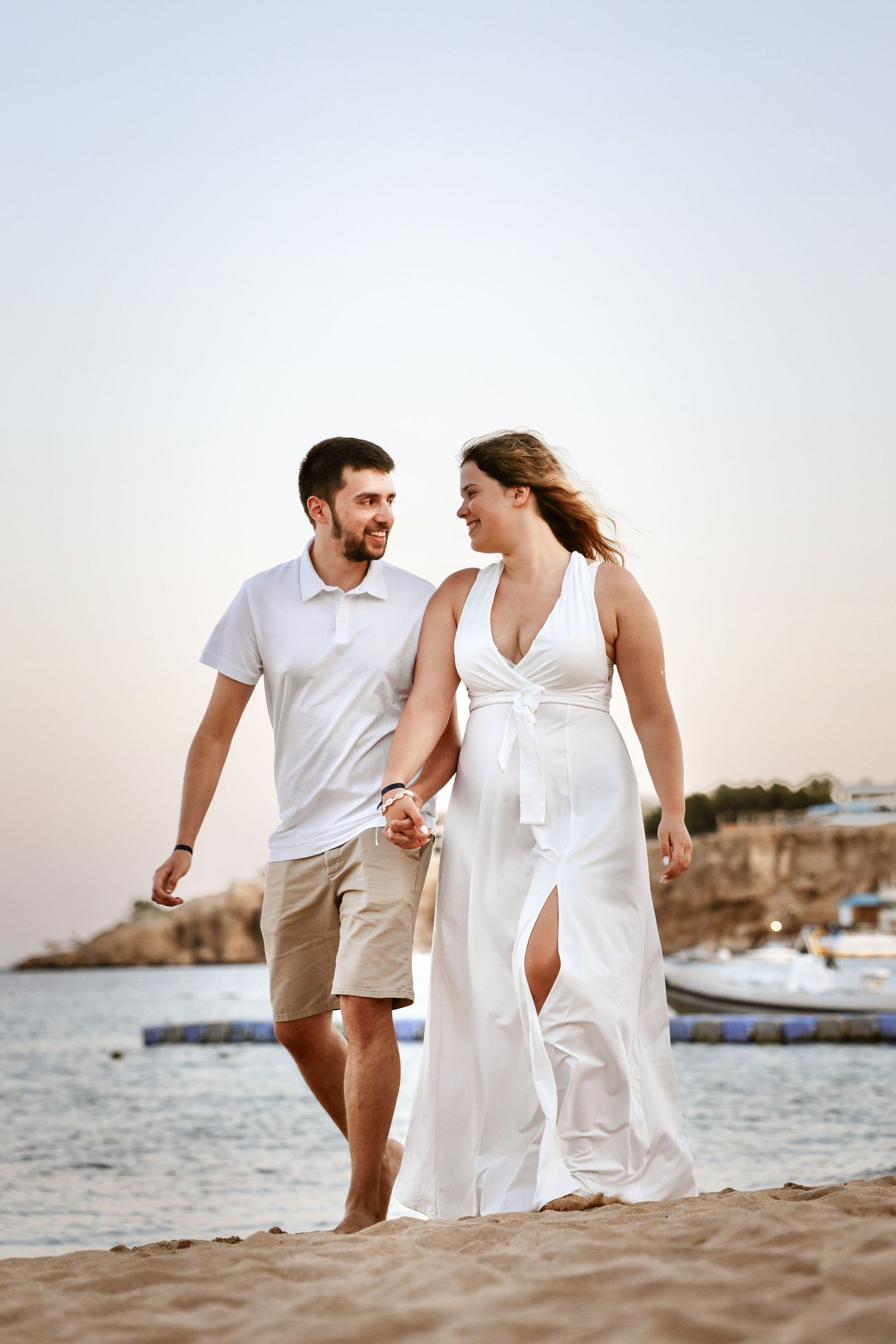 Smiling couple walking hand in hand along a sandy beach at dusk by the sea.