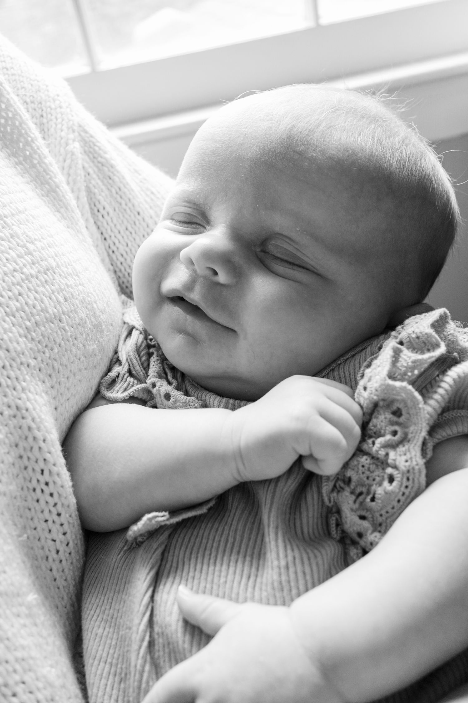 Black and white photo of a peaceful sleeping newborn baby cradled in an adult's arms near a window.