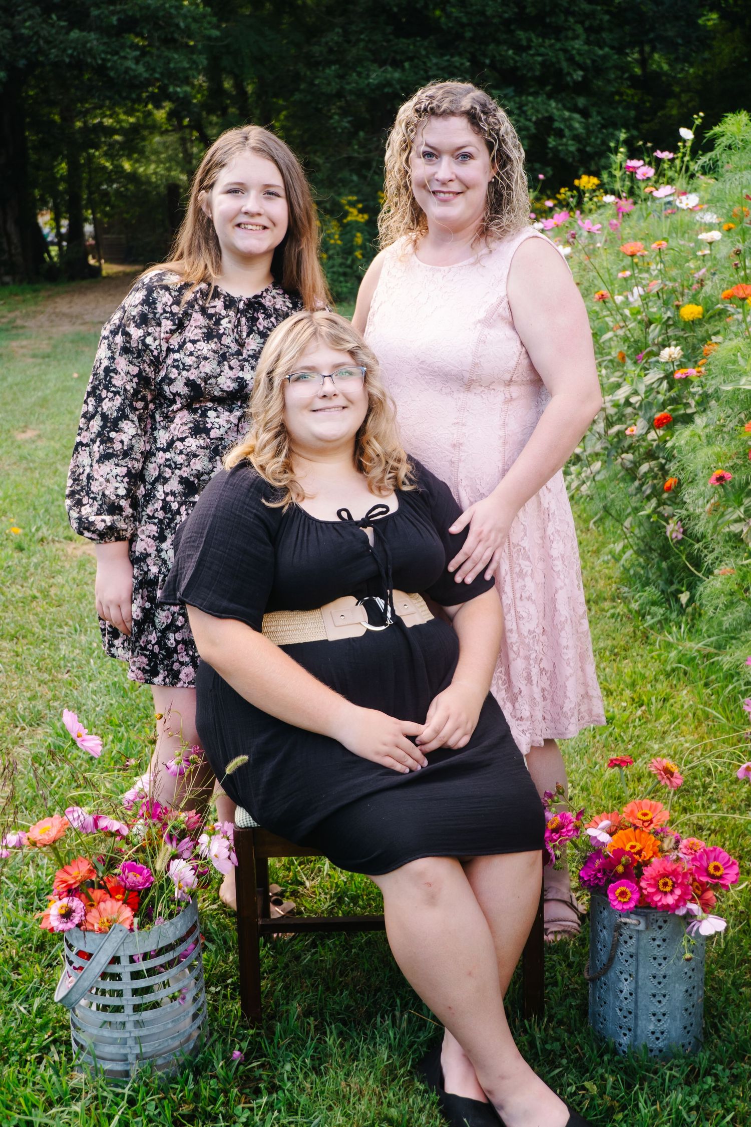 Three women posing together outdoors in garden surrounded by colorful pink and orange flowers.