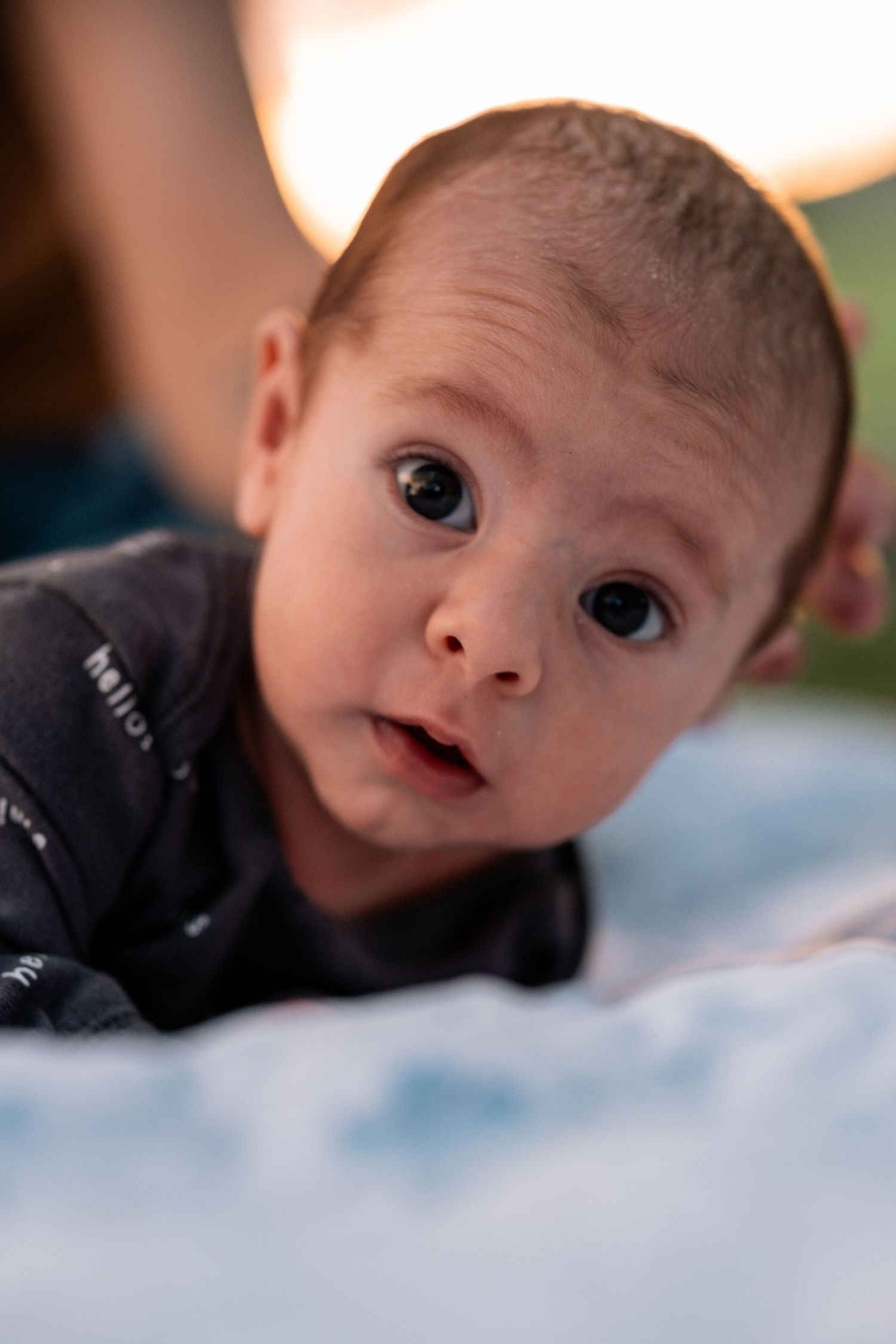 Close-up portrait of an alert newborn baby with wide eyes lying on a soft white blanket.