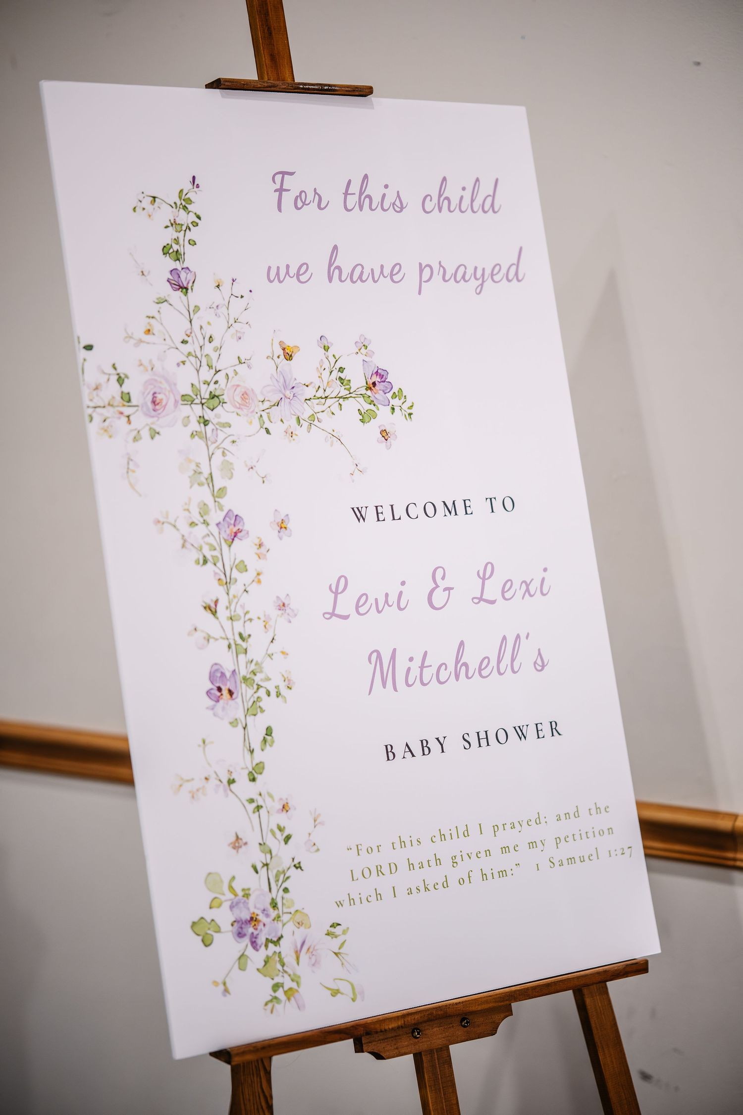 Elegant baby shower welcome sign on wooden easel for Levi & Lexi Mitchell, adorned with delicate floral cross design.