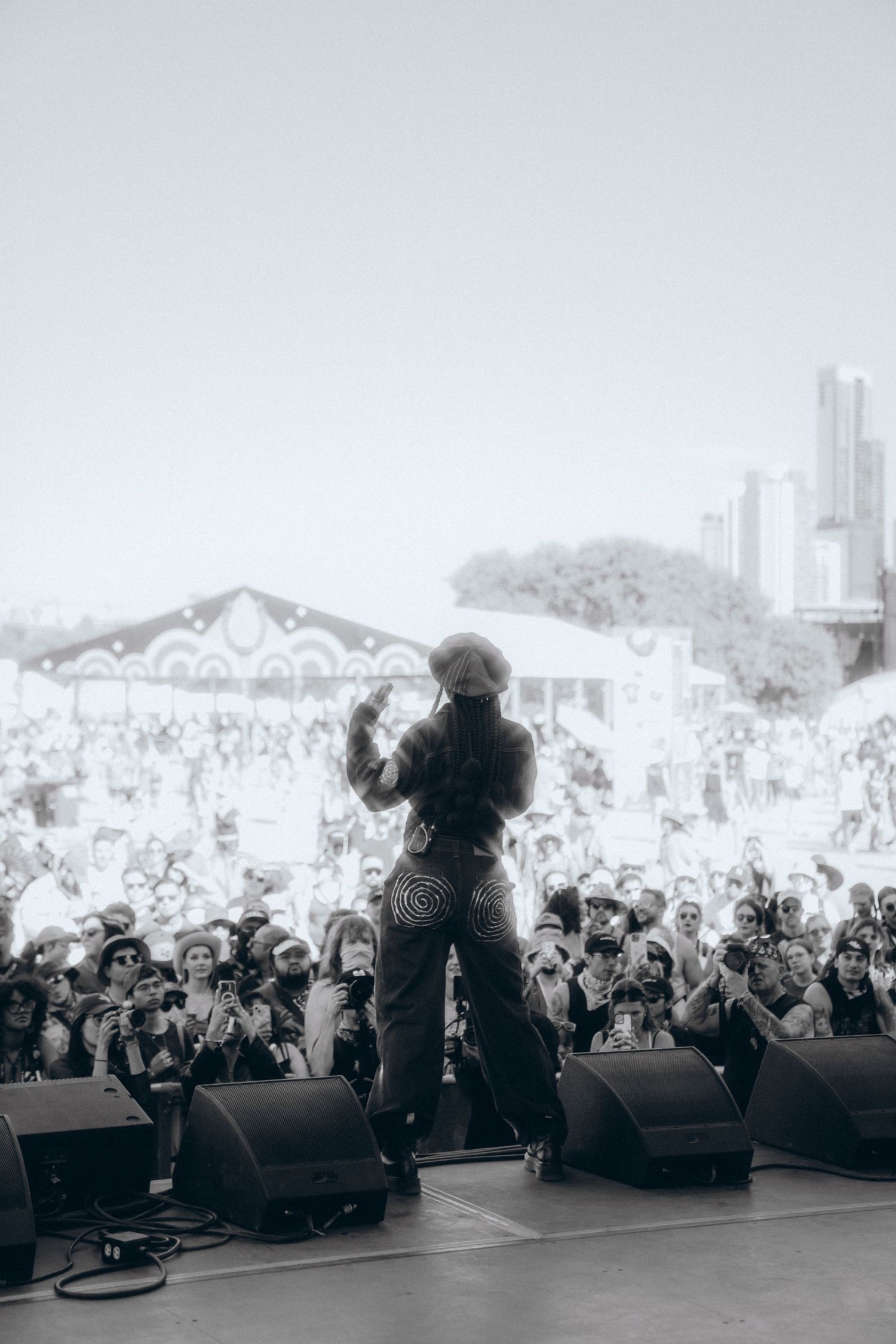 Black and white panoramic photo showing a large crowd at an outdoor concert with performers on stage in silhouette.