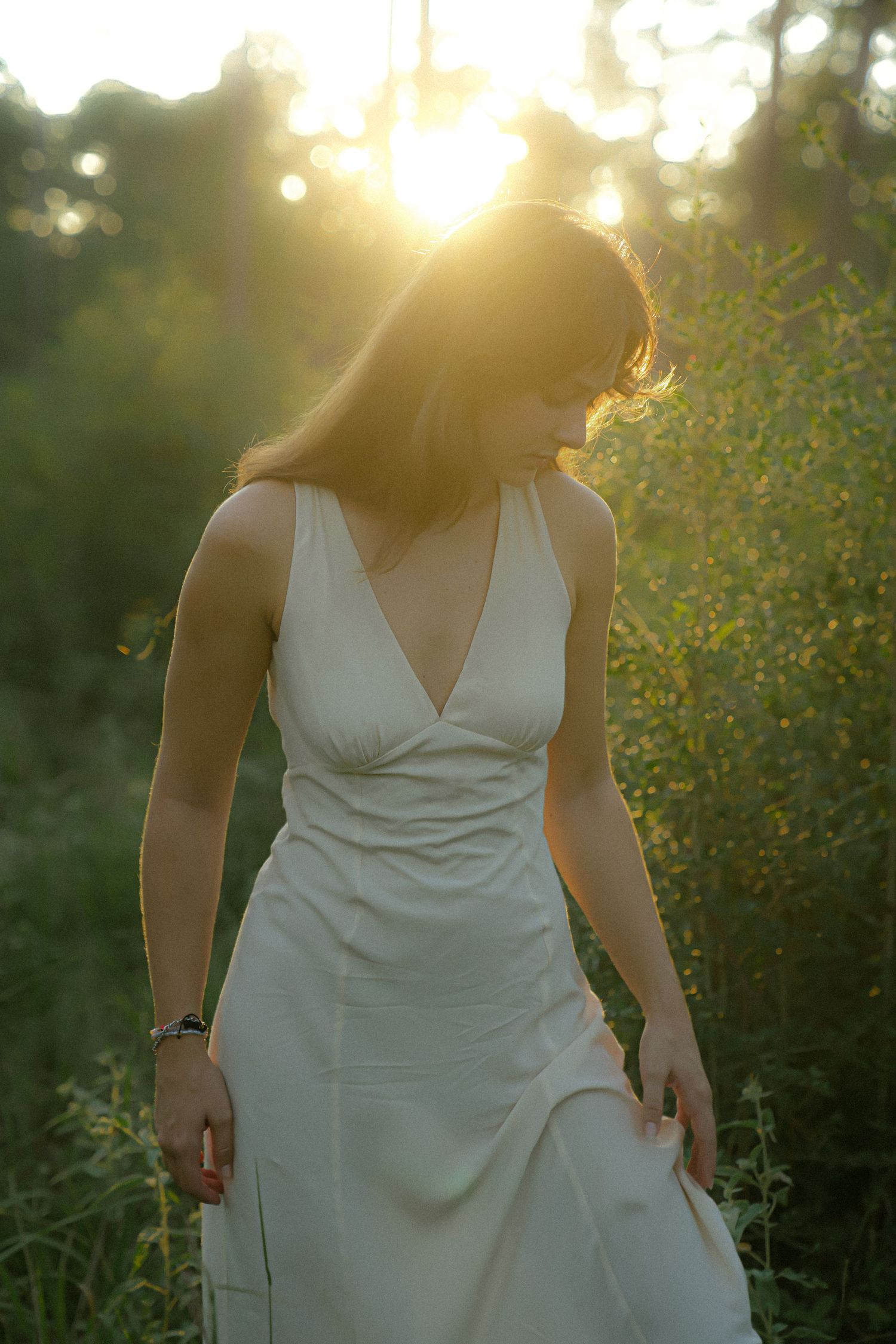 Dreamy sunset silhouette in flowing white dress against golden forest light.