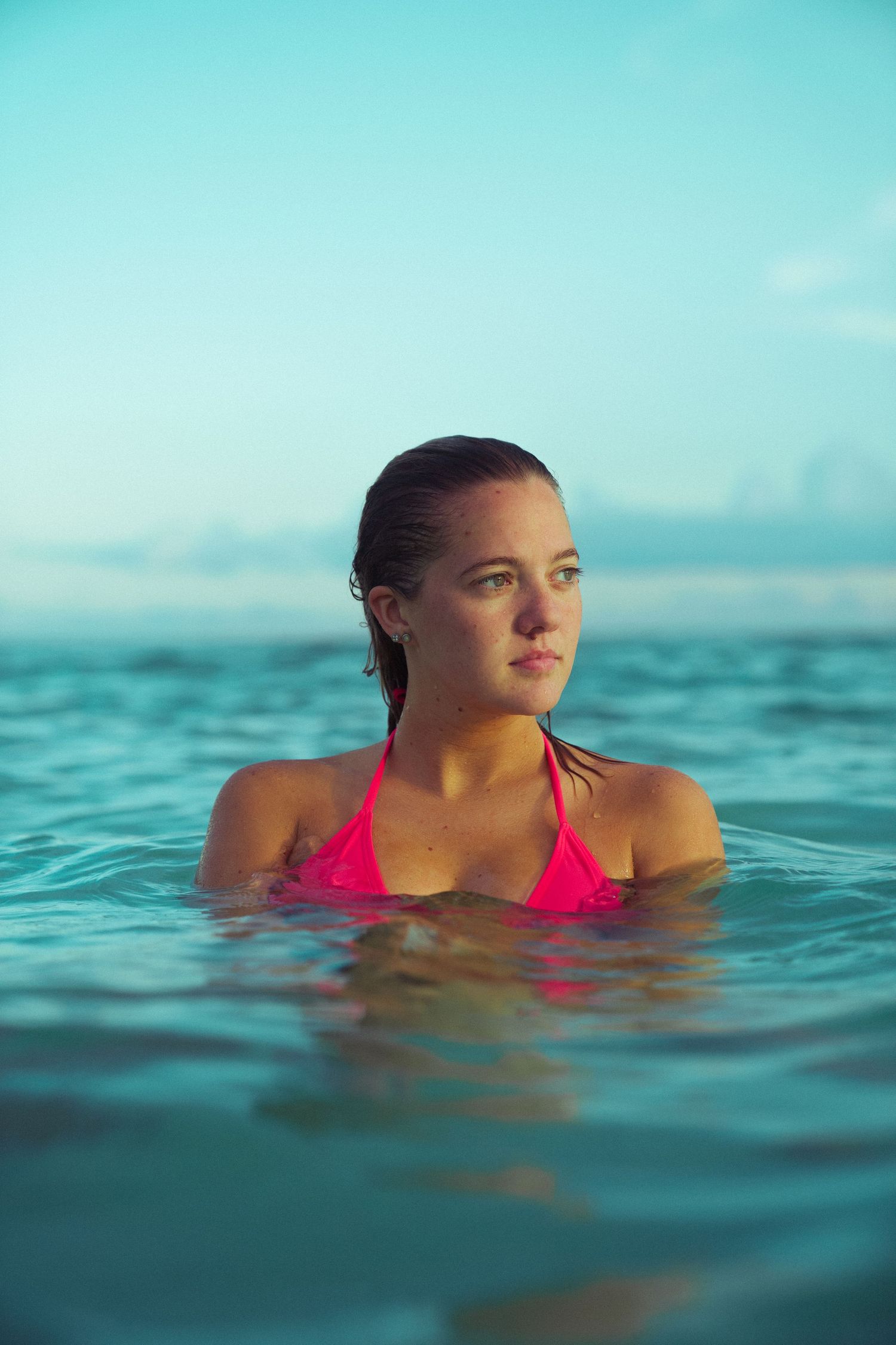 Person wearing red swimsuit poses in crystal clear ocean water against blue sky.