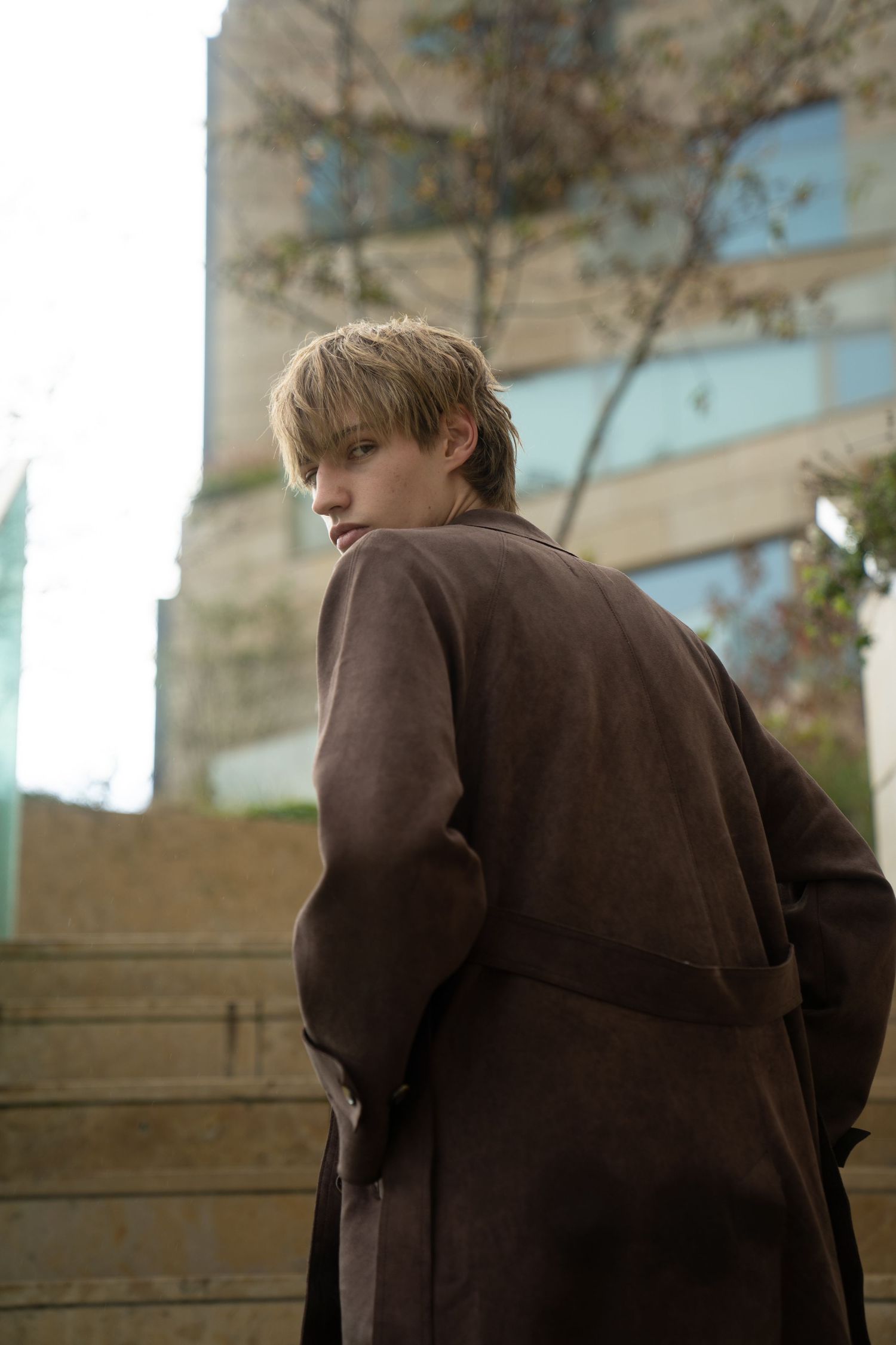 A person in a brown jacket stands outdoors looking downward in a sequence of similar poses.
