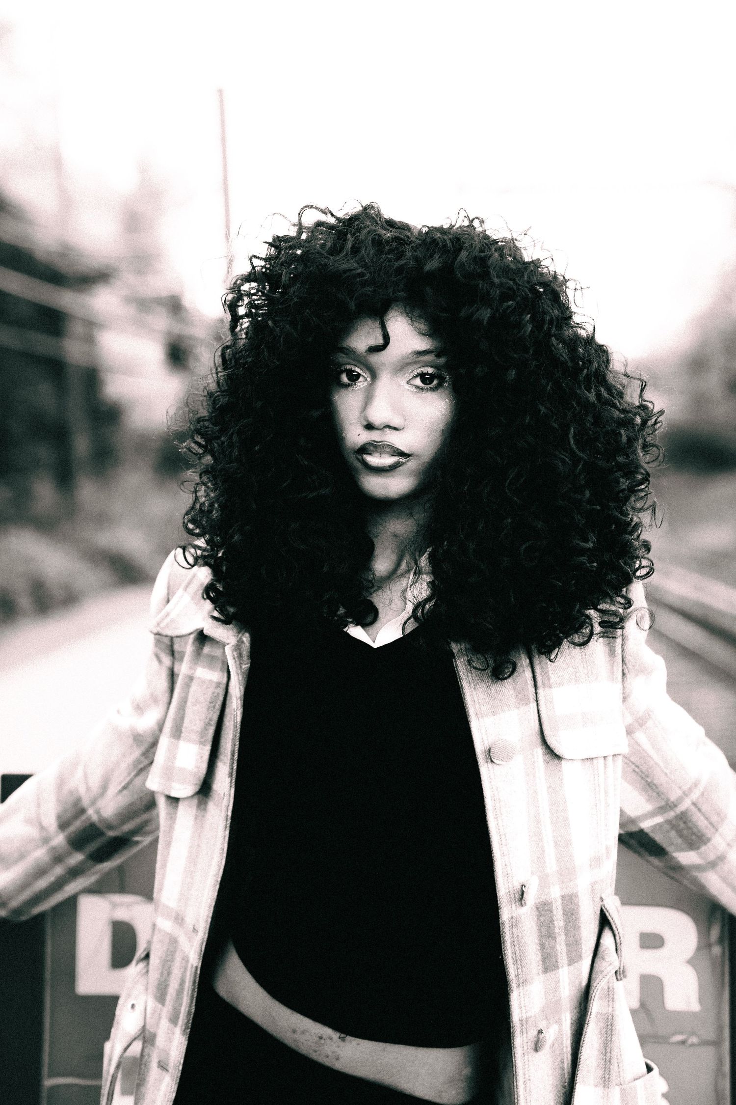 Black and white portrait of someone with voluminous natural curly hair wearing a light jacket over dark top.