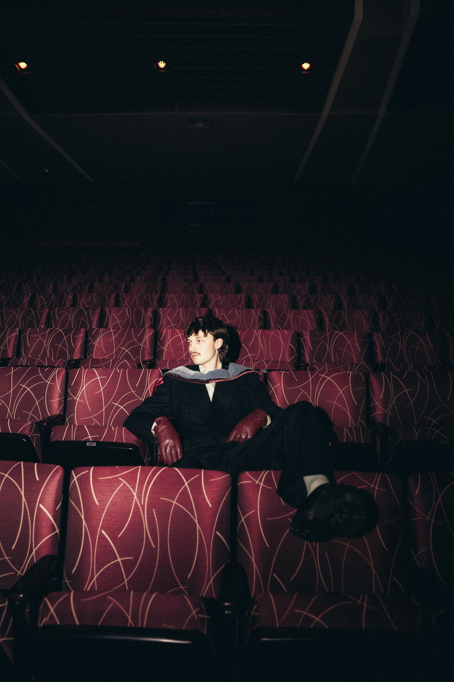 A dark silhouette sits in a movie theater with illuminated red seats creating a dramatic atmospheric scene.