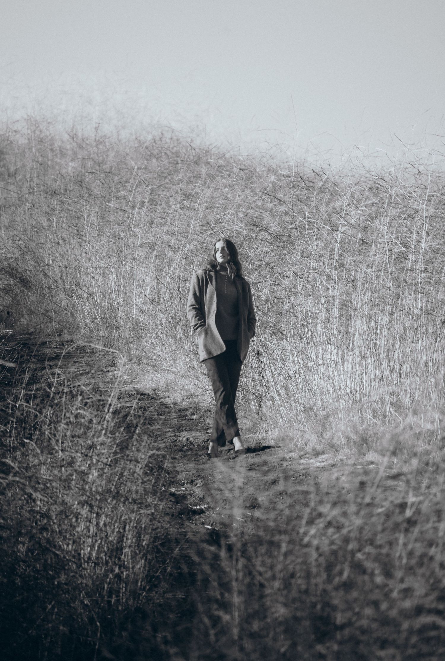 A sequence of black and white photos showing a solitary figure walking through tall grass in a moody landscape.