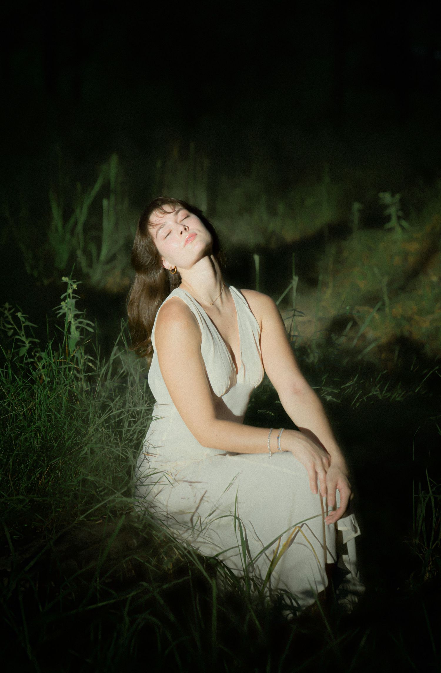 Artistic nighttime portrait in tall grass with moody lighting and a white dress.