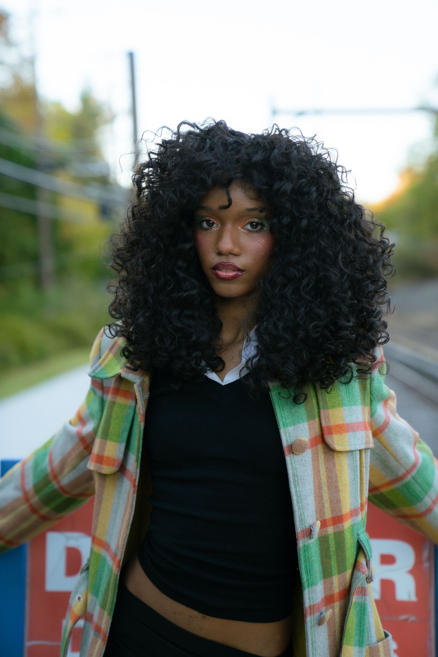 Fashion portrait featuring curly hair and a plaid green jacket against a blue background with red lettering.
