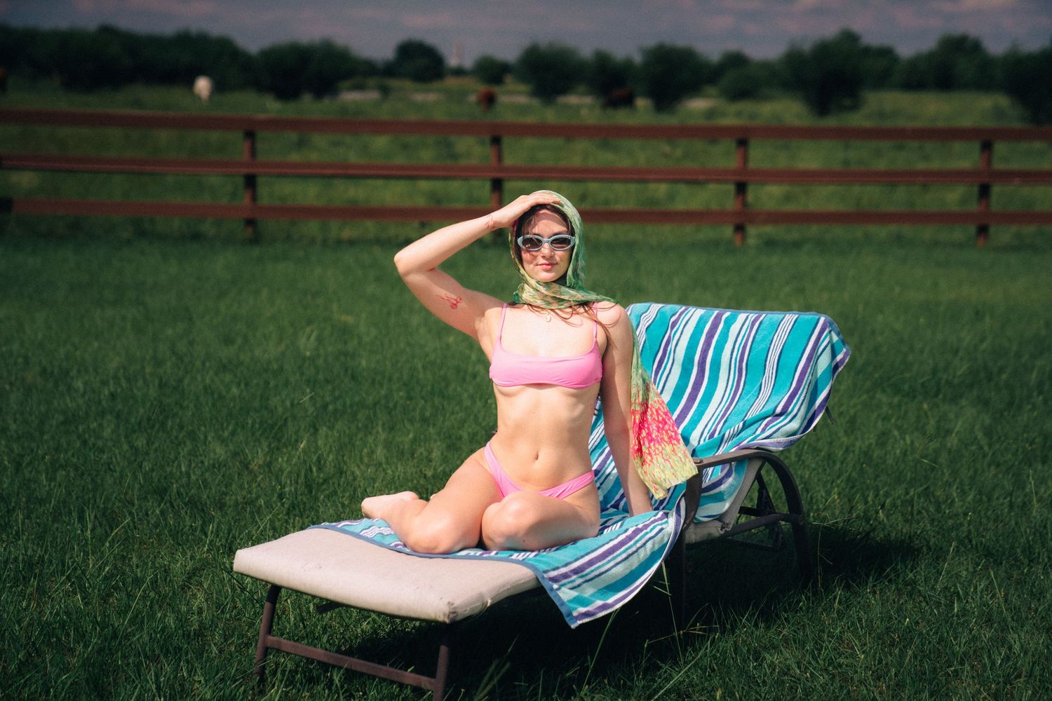Colorful beach towel draped over lounge chair on green lawn with wooden fence in background at sunset.