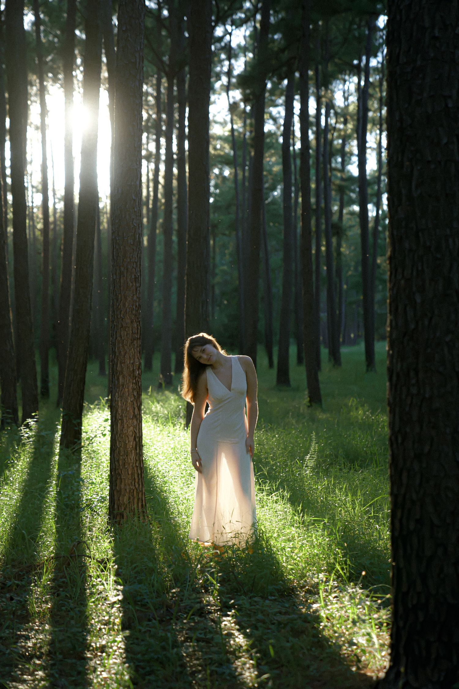 Ethereal portrait in a sunlit forest with dramatic light beams filtering through tall trees.